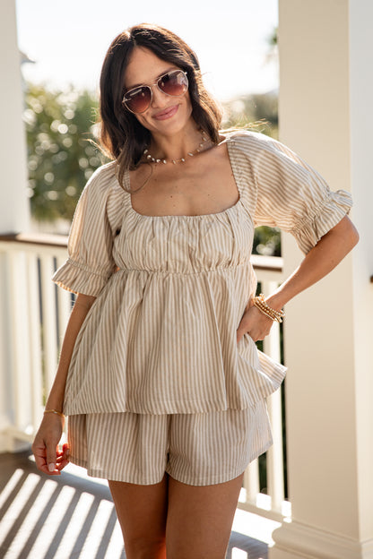 Woman wearing a beige striped outfit with sunglasses on a sunny day.