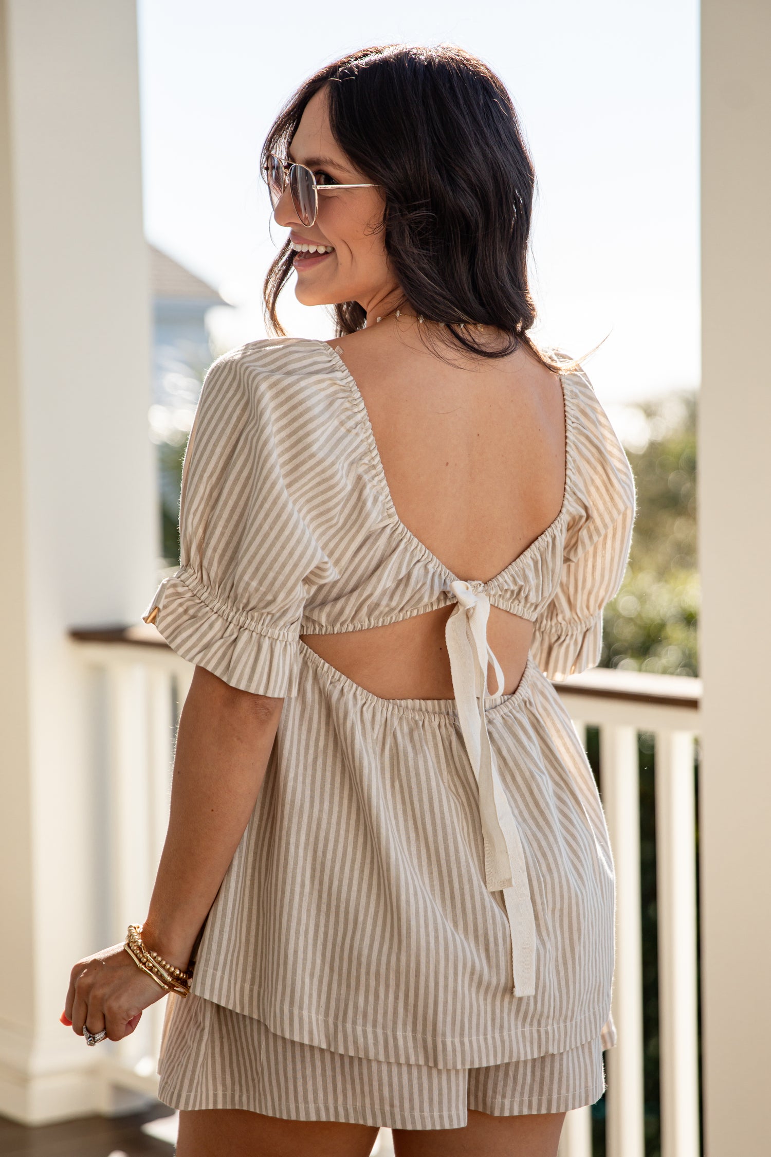Woman wearing a light-colored striped outfit with an open back on a balcony.