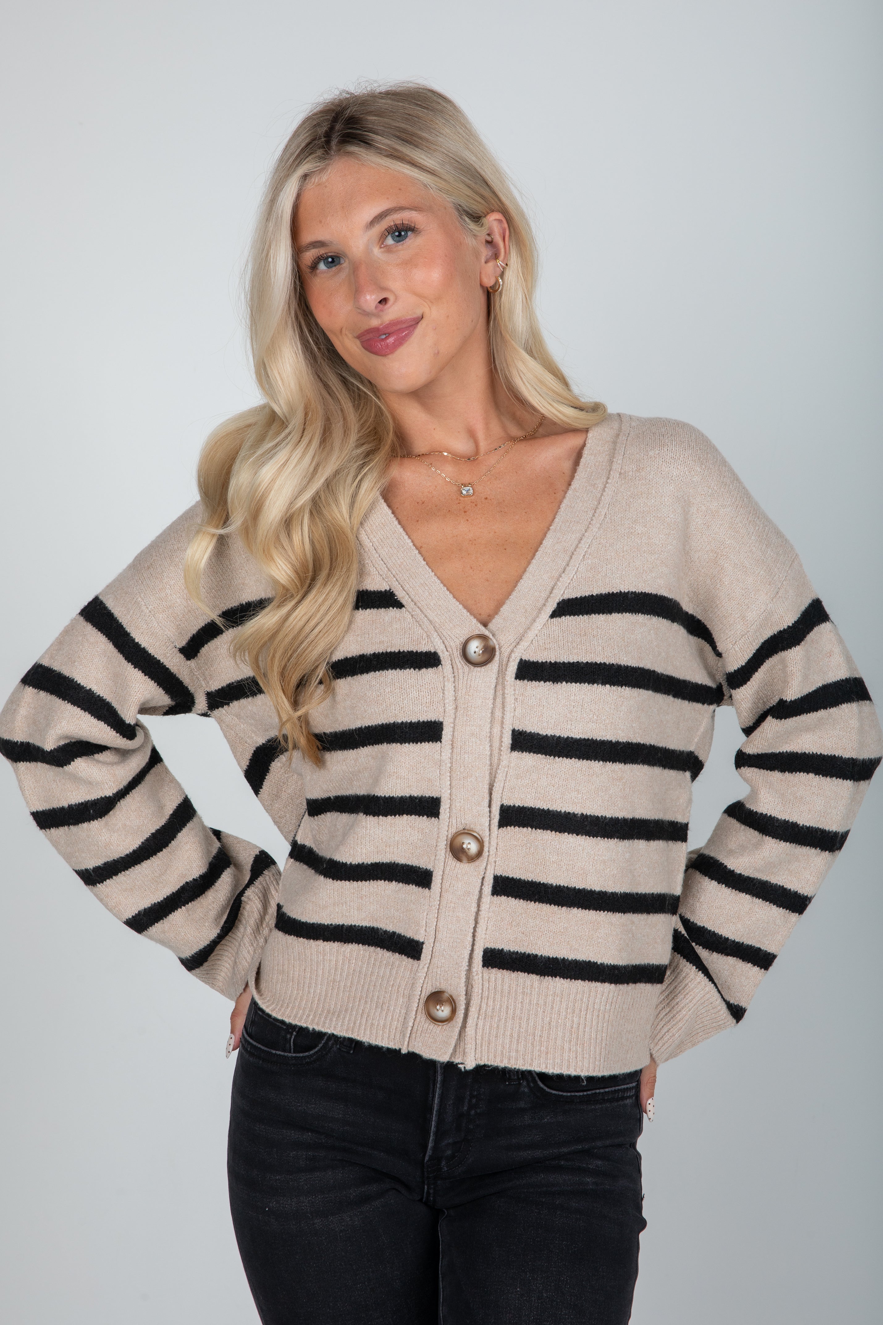 Woman wearing a beige cardigan with black stripes on a plain background