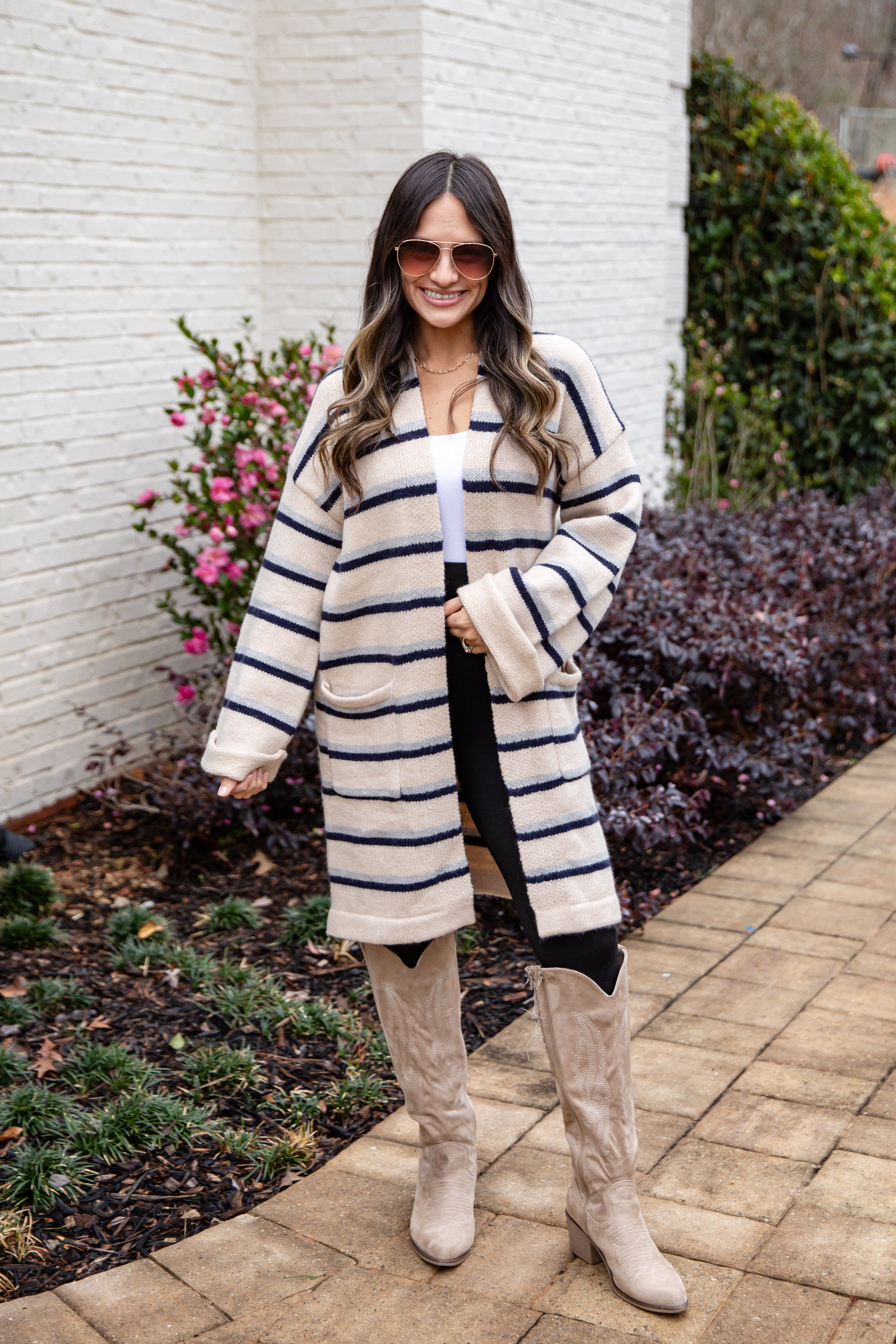 Woman wearing a long striped coat and knee-high boots standing outdoors.