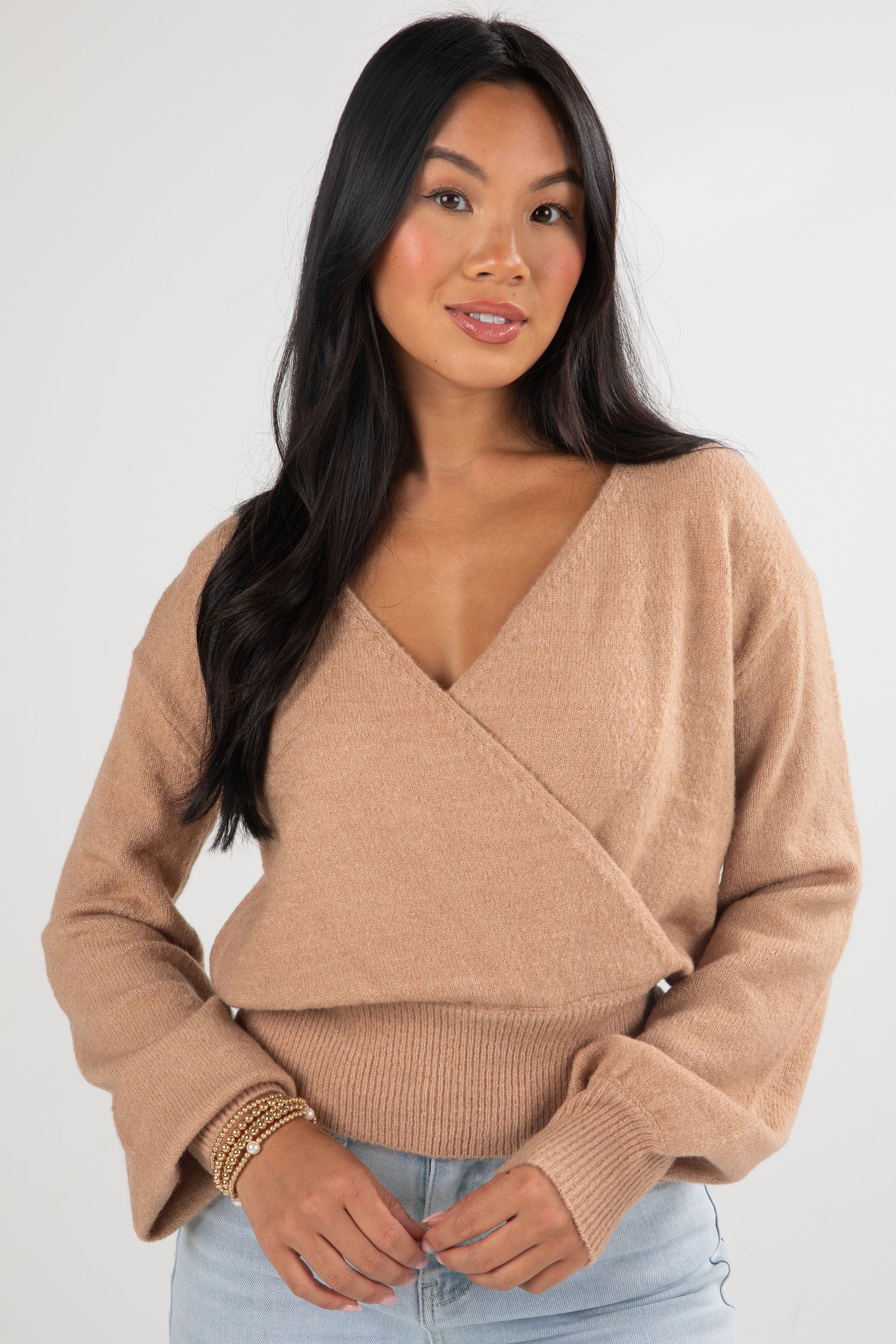 Woman wearing a beige wrap sweater against a white background