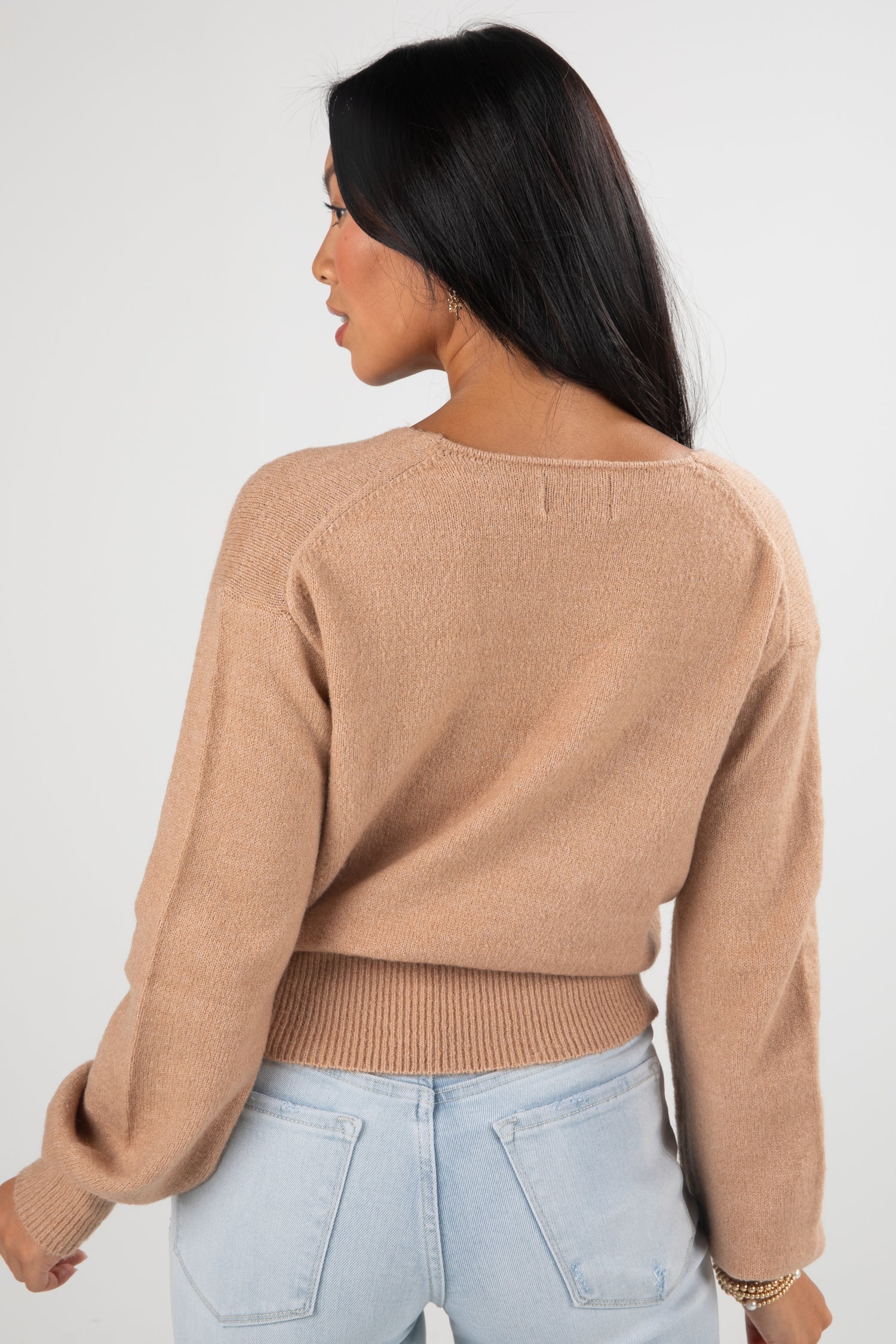 Woman wearing a beige sweater and light blue jeans against a white background