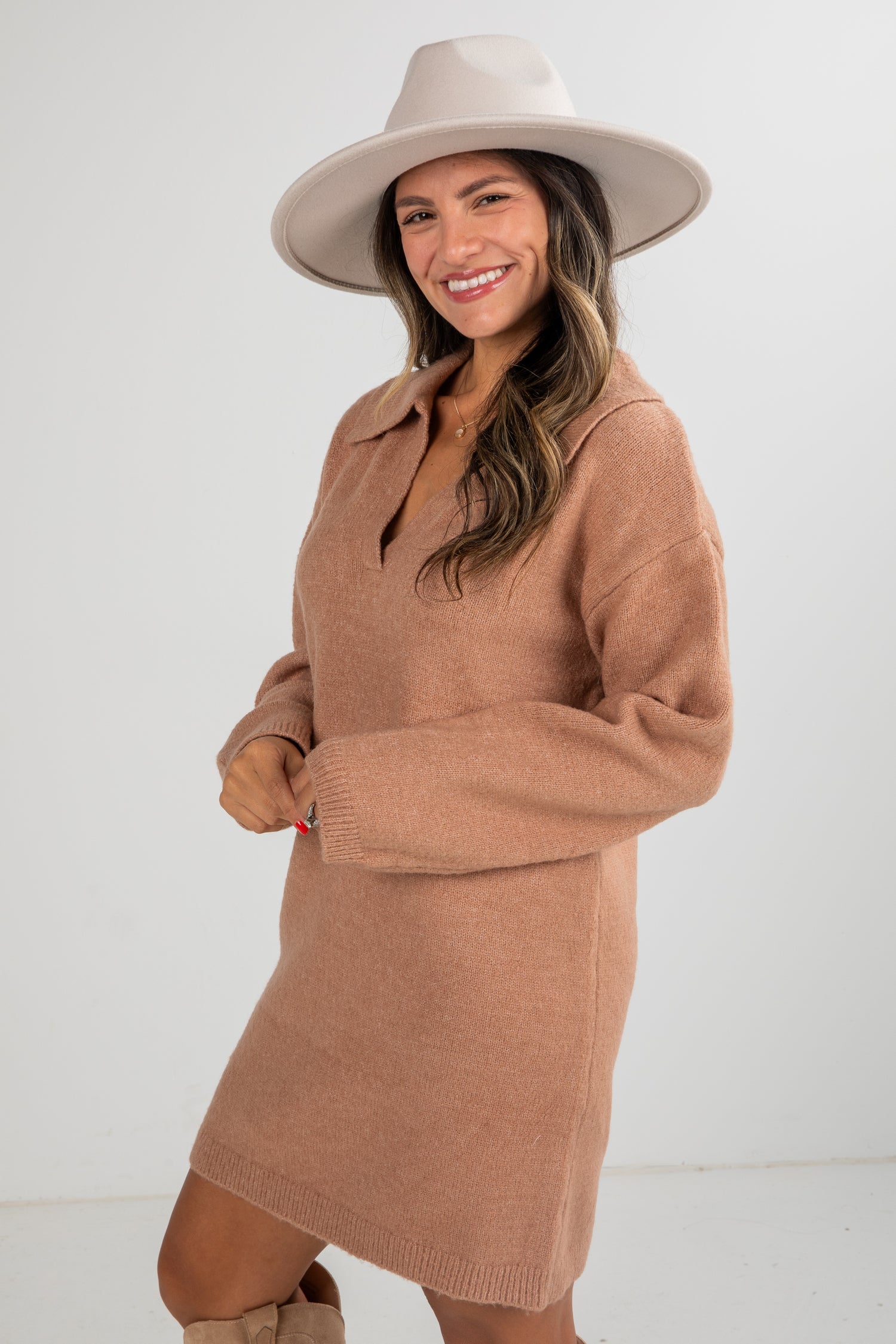 Woman wearing a brown sweater dress and beige hat on a white background