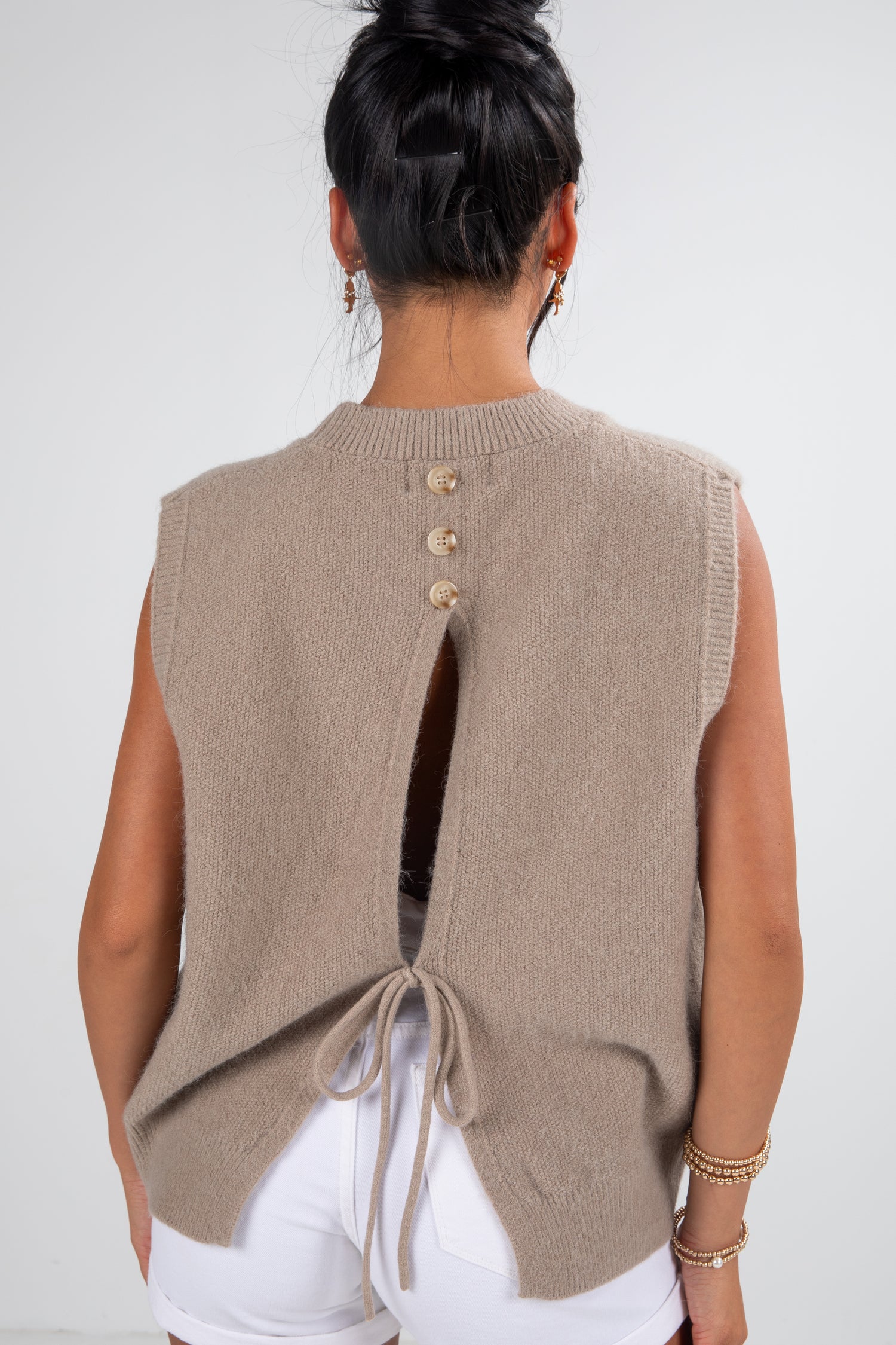 Person wearing a beige sleeveless knitted vest with button details on a white background