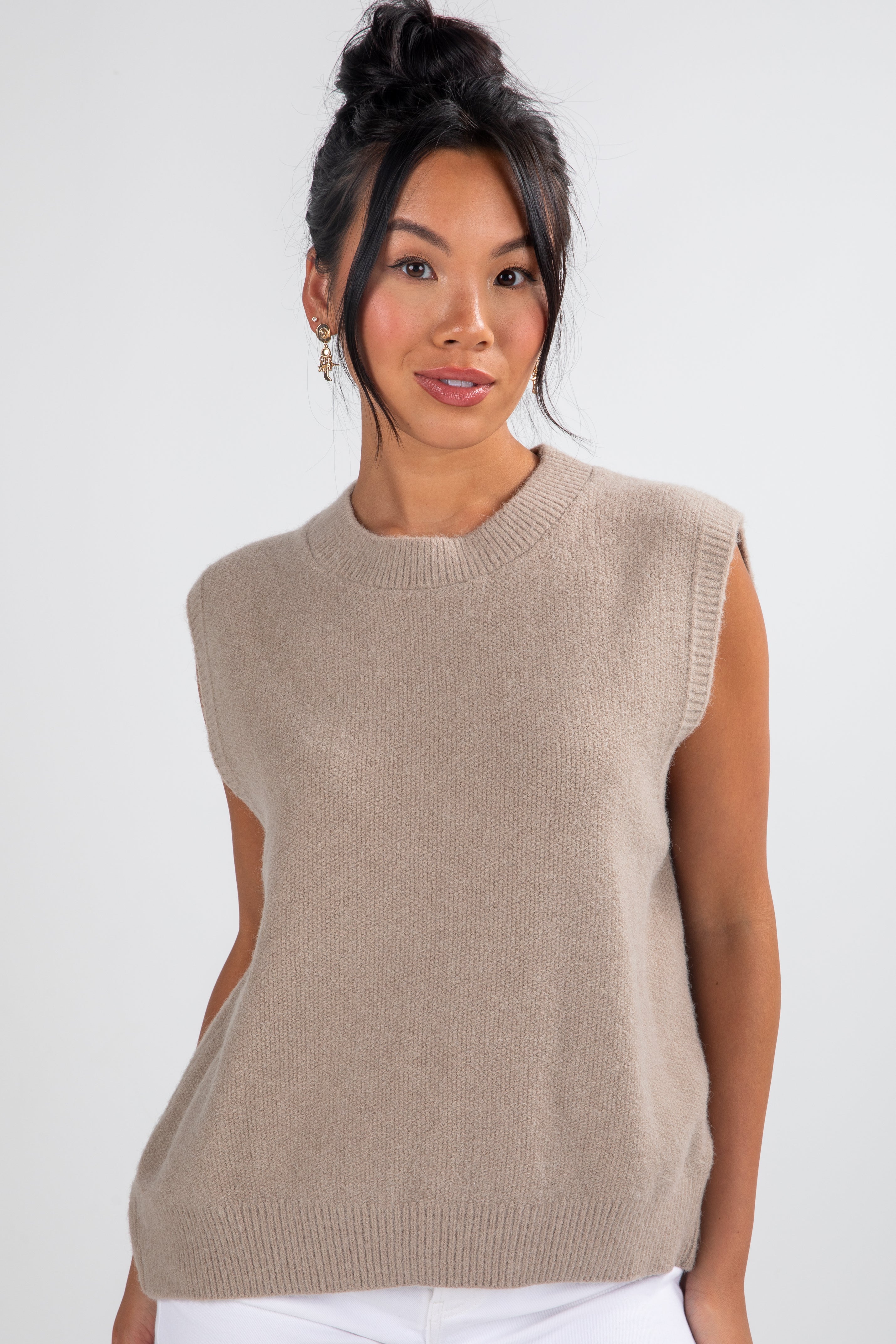 Woman wearing a beige sleeveless sweater against a white background