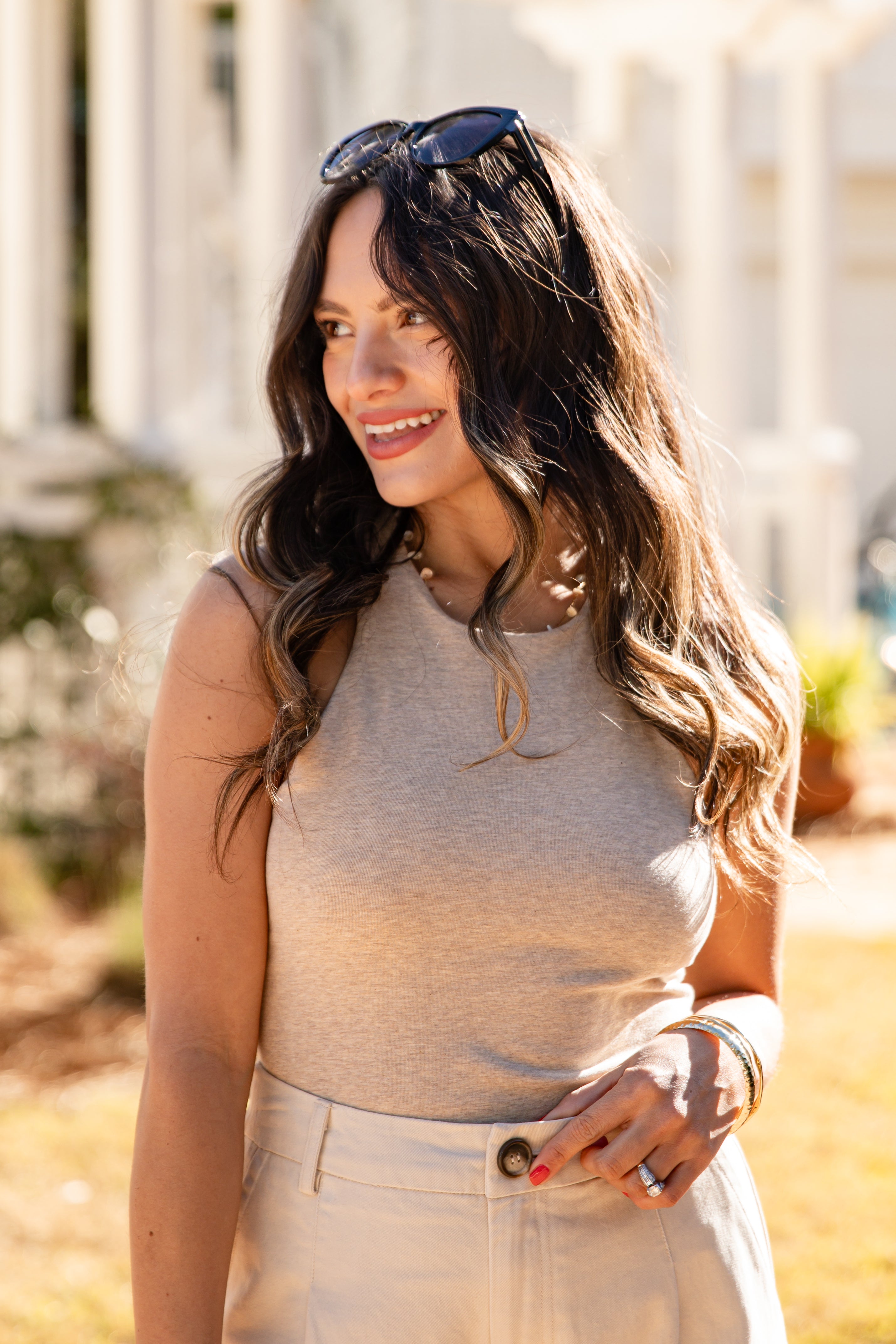 Woman wearing a gray tank top and beige pants outdoors with a blurred background