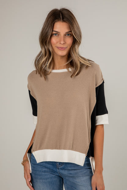 Woman wearing a beige and black color-blocked top with blue jeans on a plain background