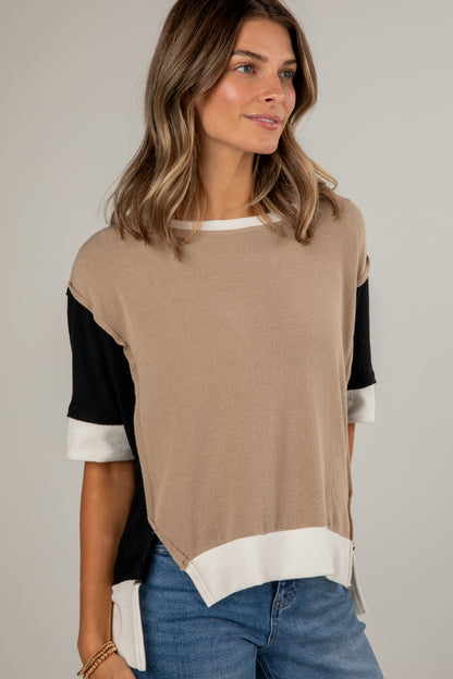 Woman wearing a beige and black top with white trim on a plain background