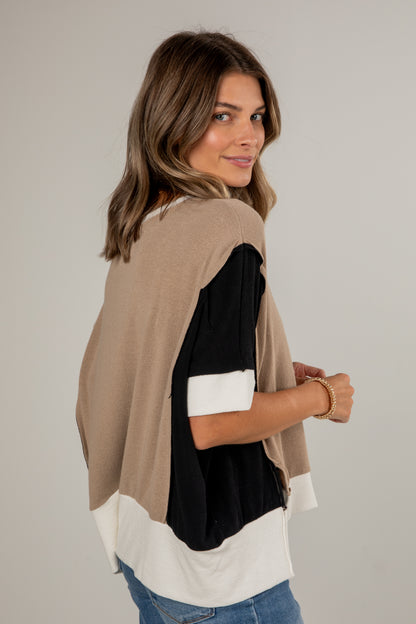Woman wearing a layered outfit with a beige cardigan, black top, and white shirt on a plain background