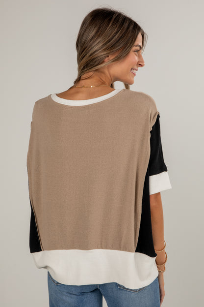 Woman wearing a beige, black, and white top with blue jeans on a plain background