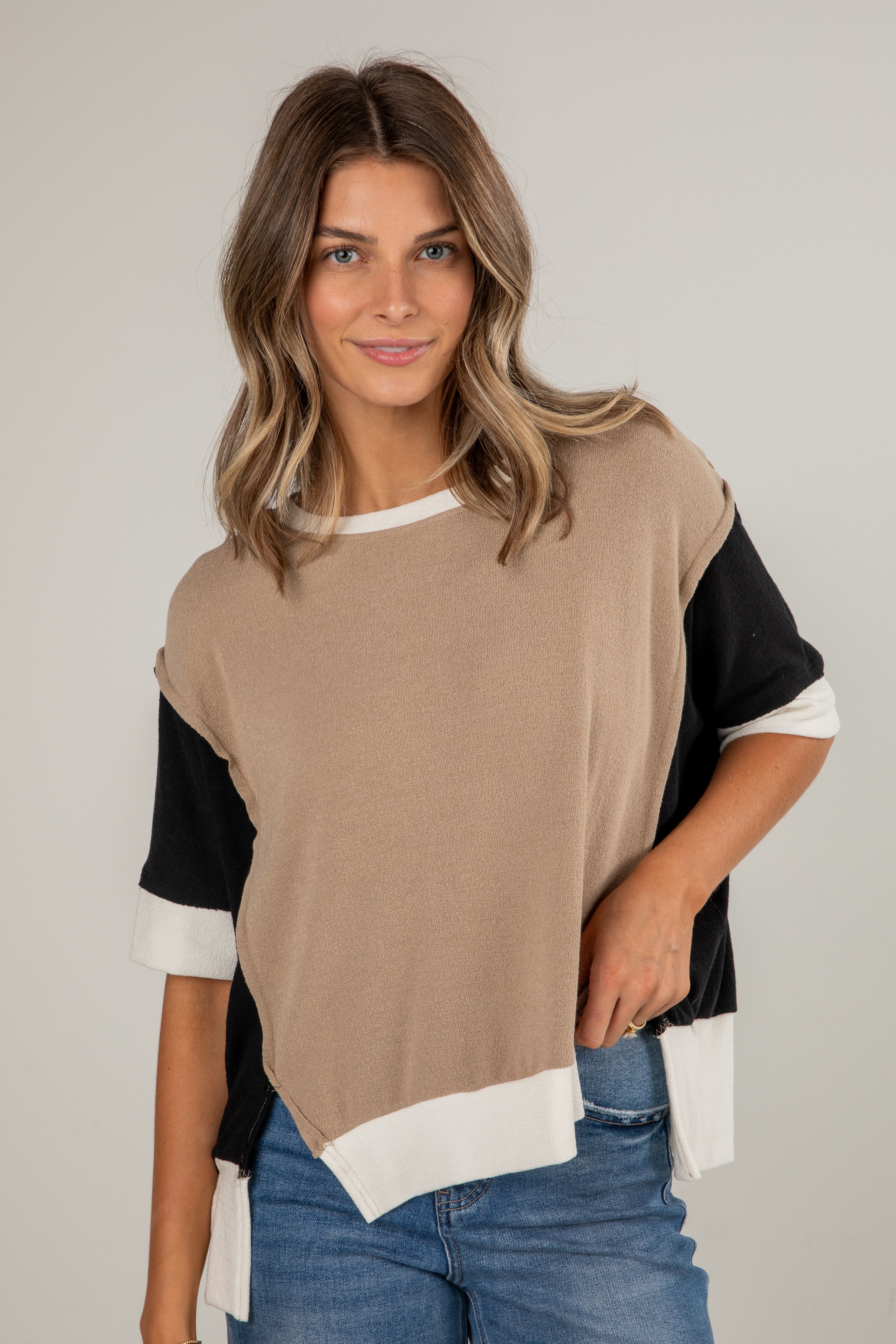 Woman wearing a beige, black, and white color-blocked top with blue jeans on a plain background