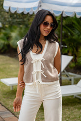 Woman wearing a patterned sleeveless top and white pants outdoors under an umbrella.