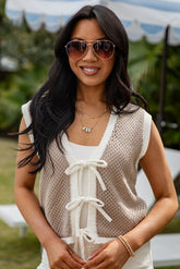 Woman wearing sunglasses and a beige top with white lace details outdoors.