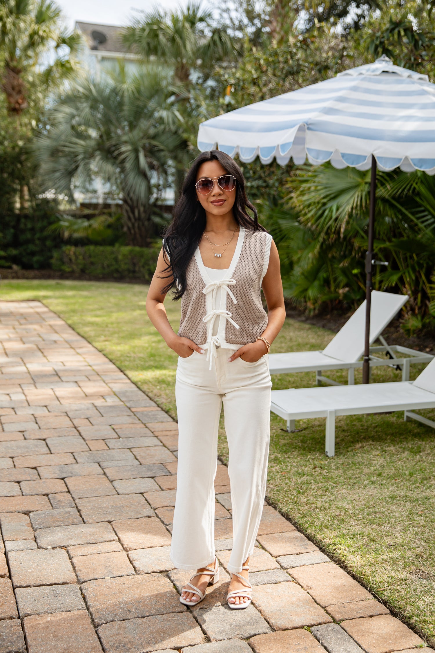 Woman in a white outfit standing on a patio with outdoor furniture and greenery in the background