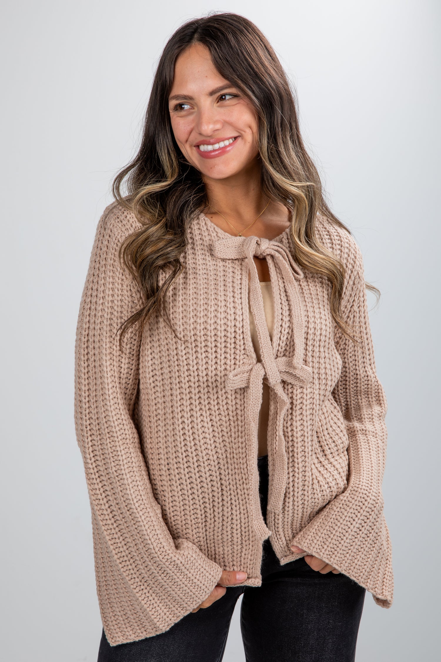 Woman wearing a beige knitted sweater with a tie detail on a plain background