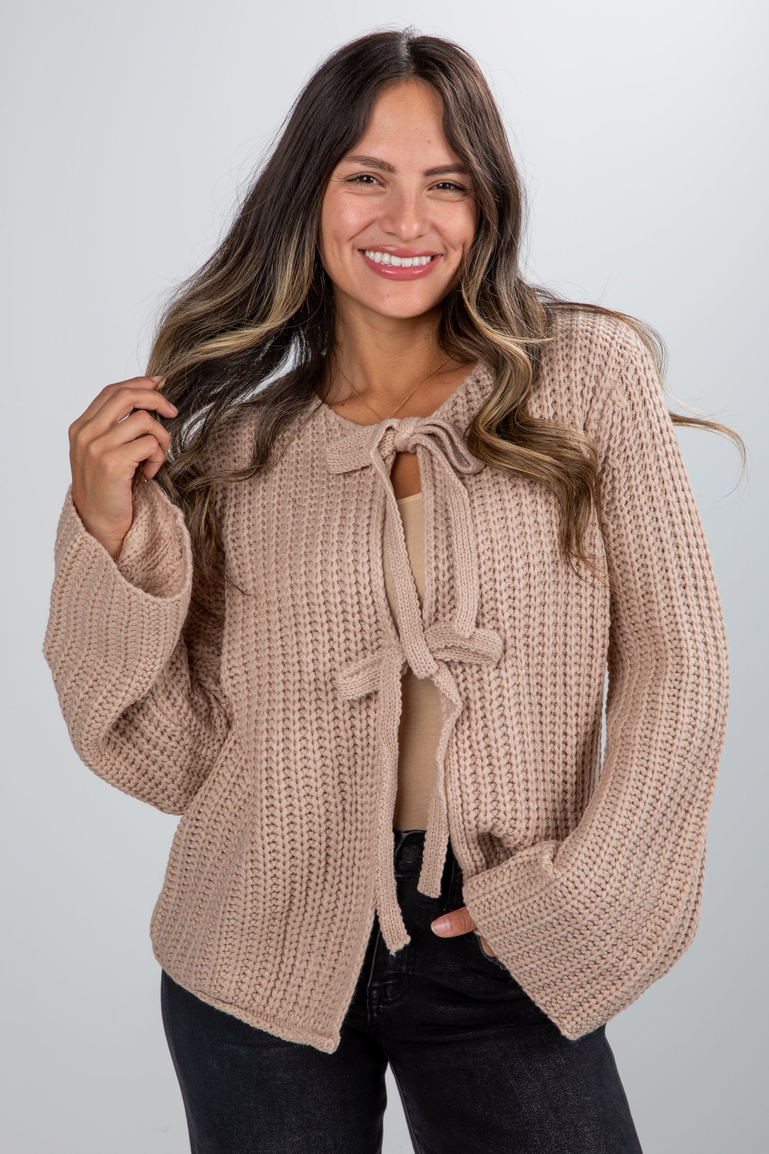 Woman wearing a beige knitted cardigan with a tie detail on a plain background