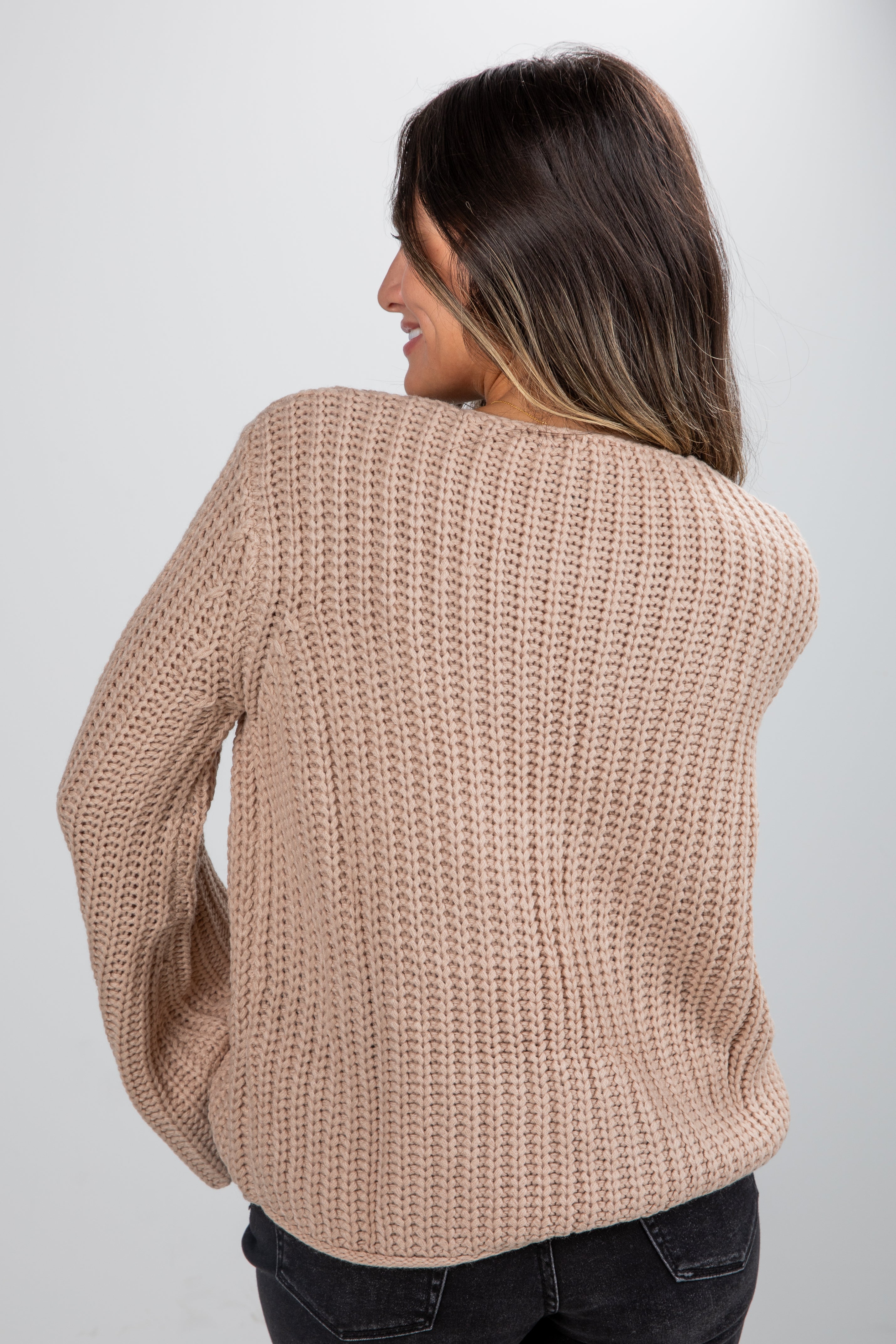 Woman wearing a beige chunky knit sweater against a plain background