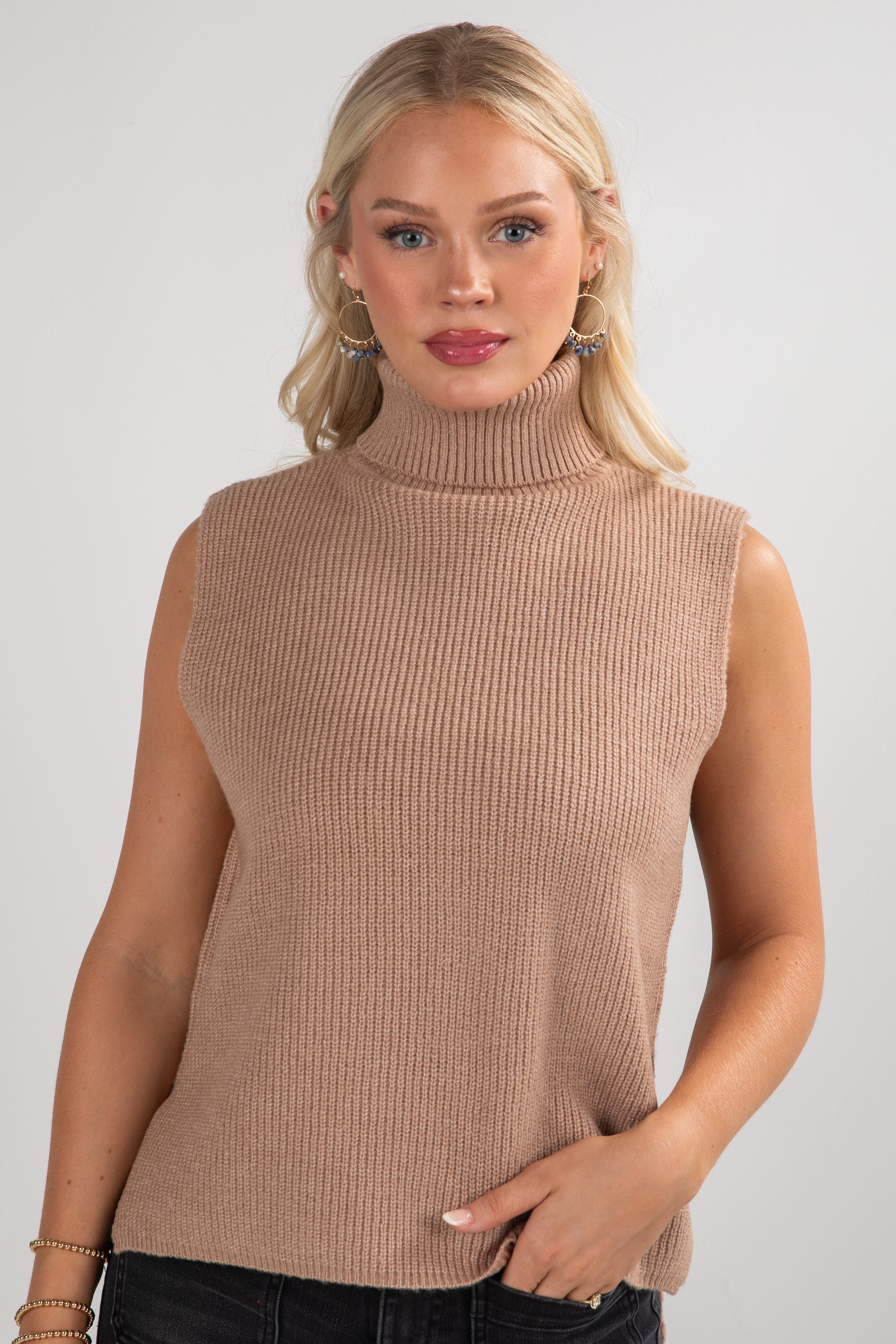Woman wearing a beige sleeveless ribbed sweater against a plain background