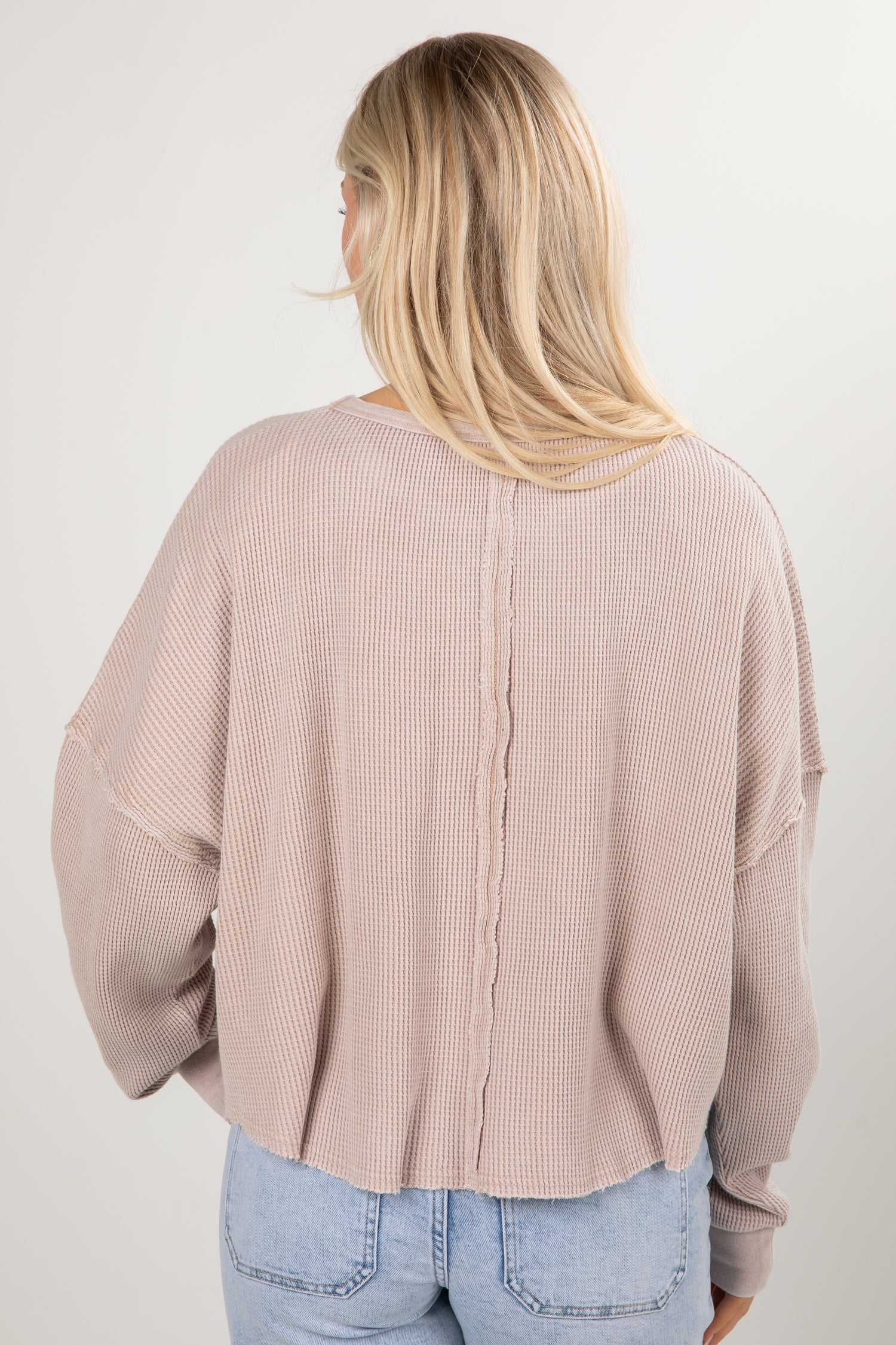 Person wearing a beige ribbed sweater and light blue jeans against a white background