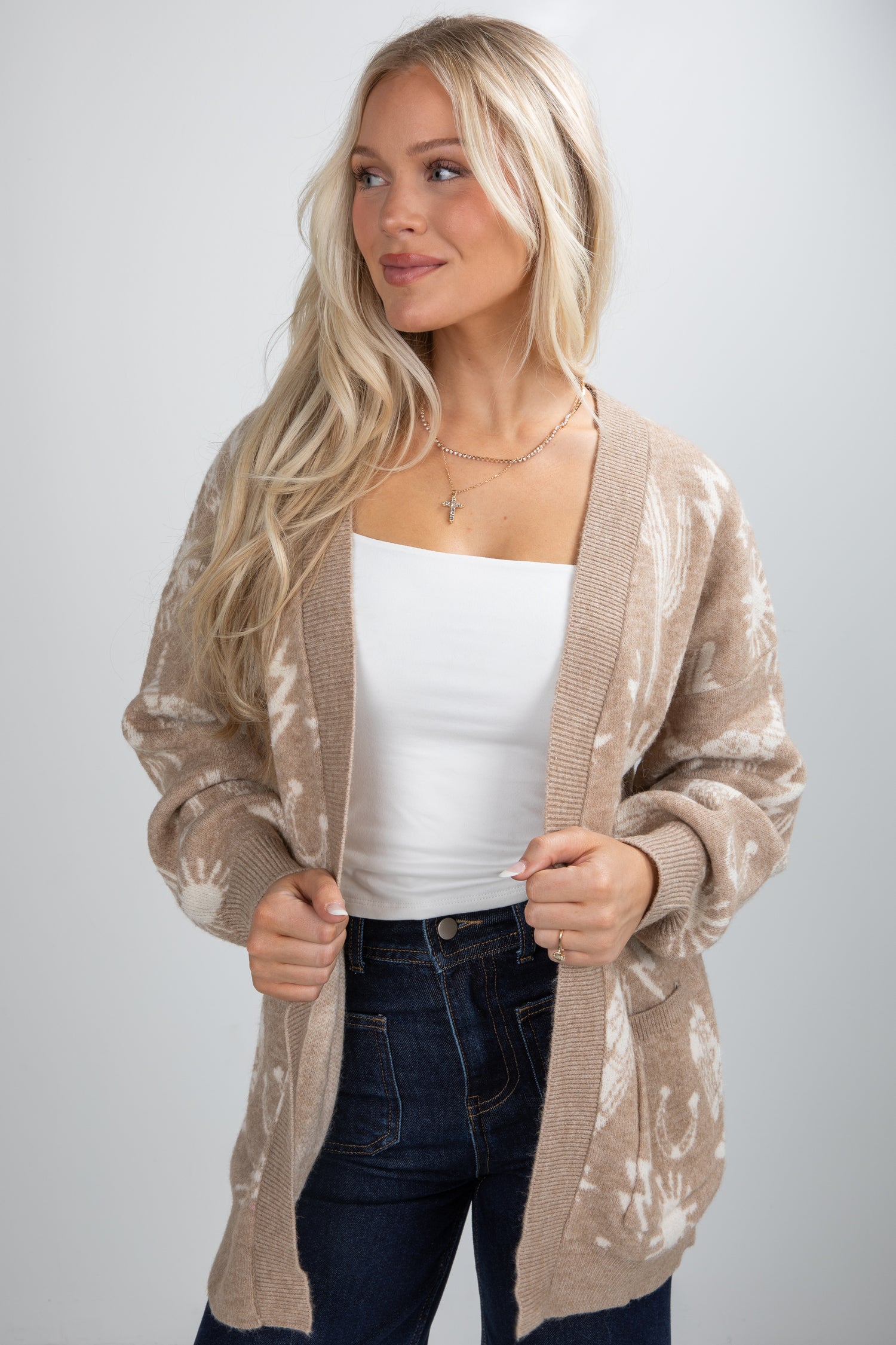 Woman wearing a beige floral cardigan over a white top and jeans on a plain background