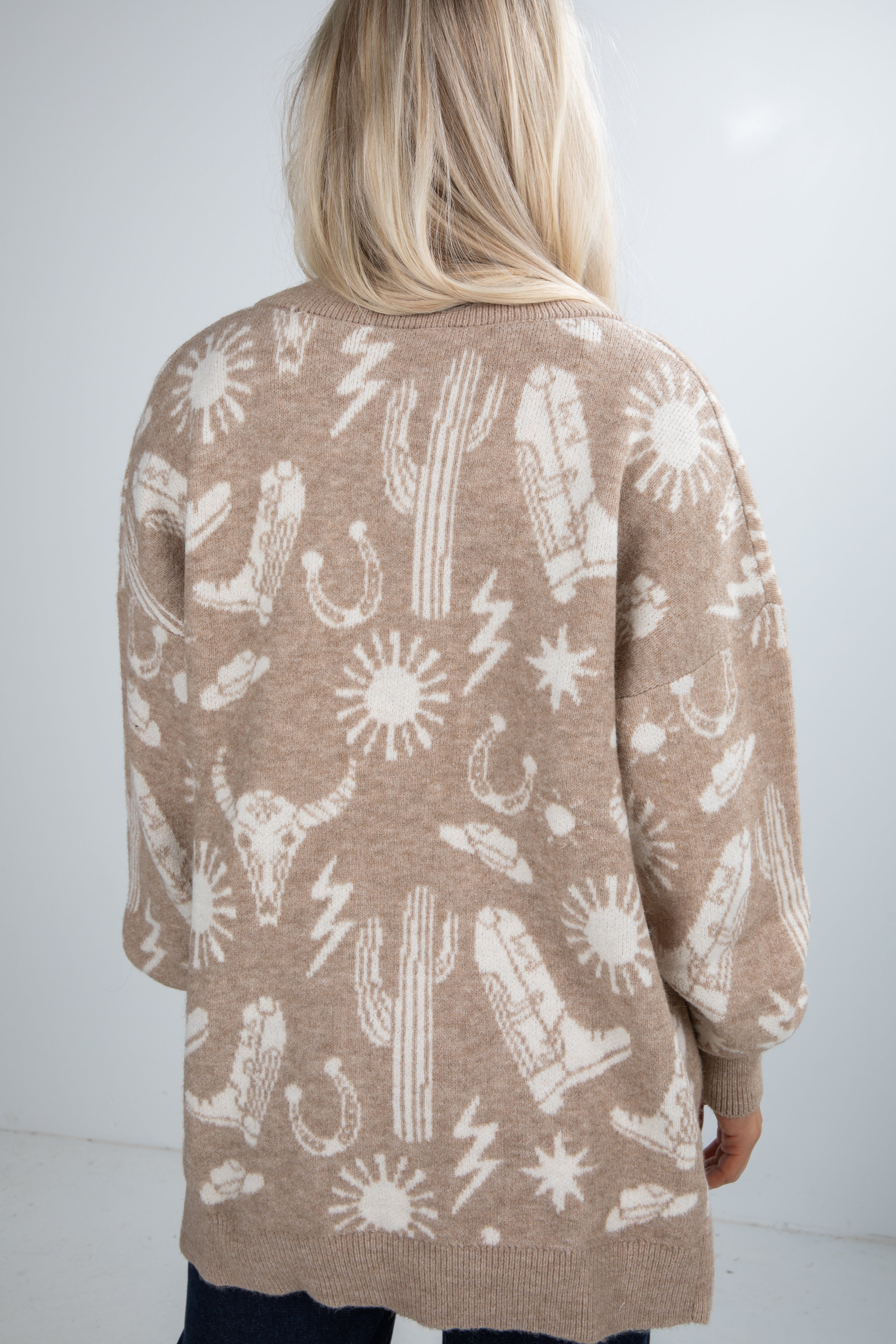 Person wearing a beige cardigan with white patterns on a plain background