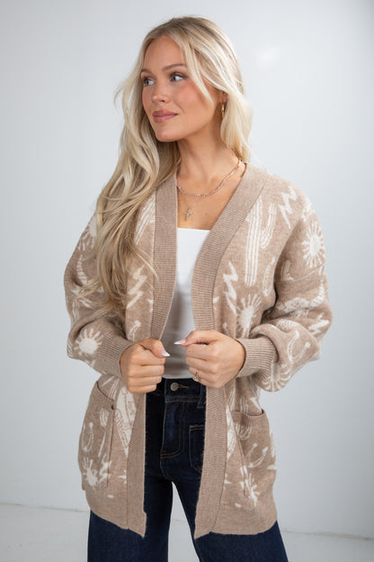 Woman wearing a beige patterned cardigan over a white top and dark jeans on a white background