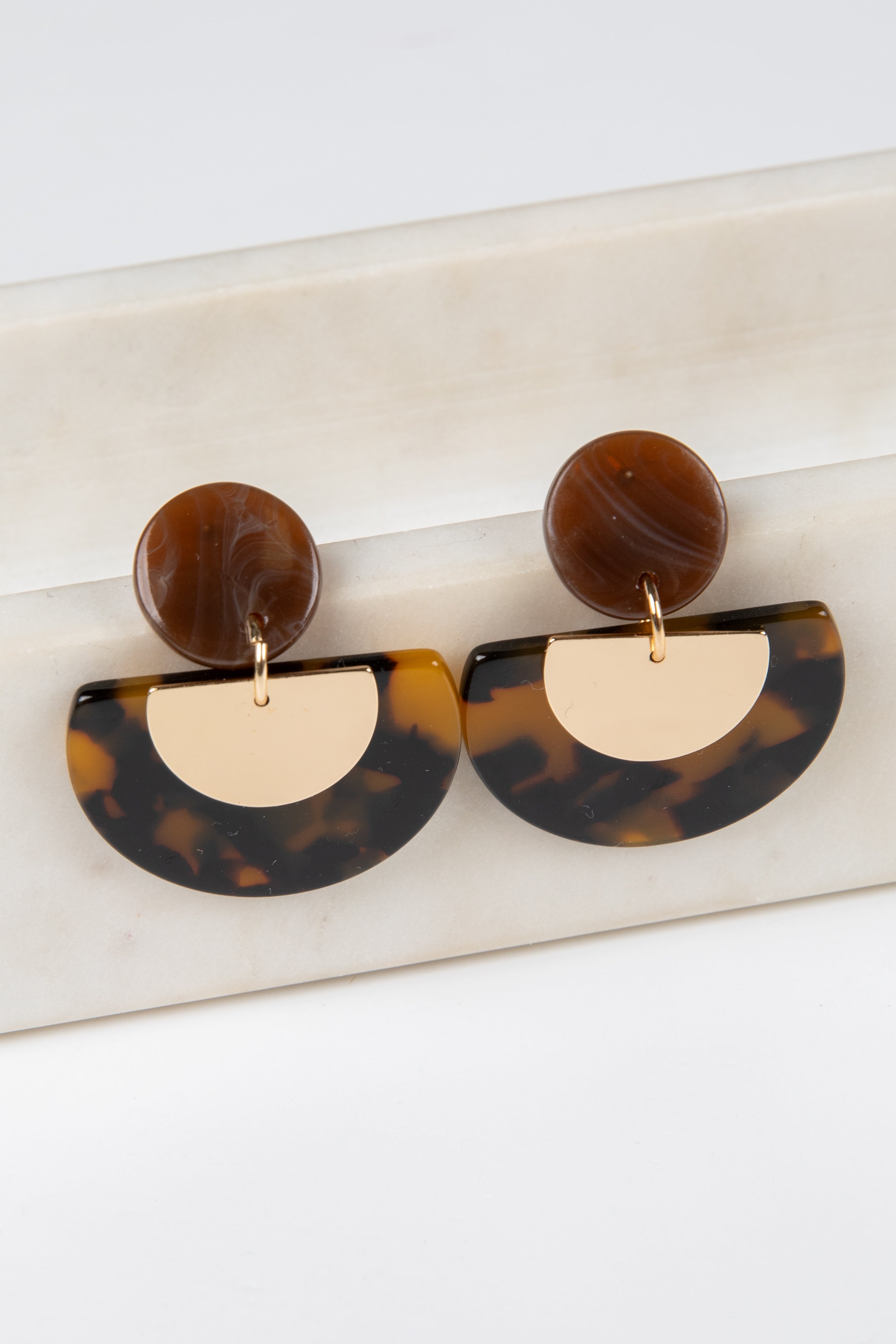 Tortoiseshell and gold half-circle earrings on a marble surface