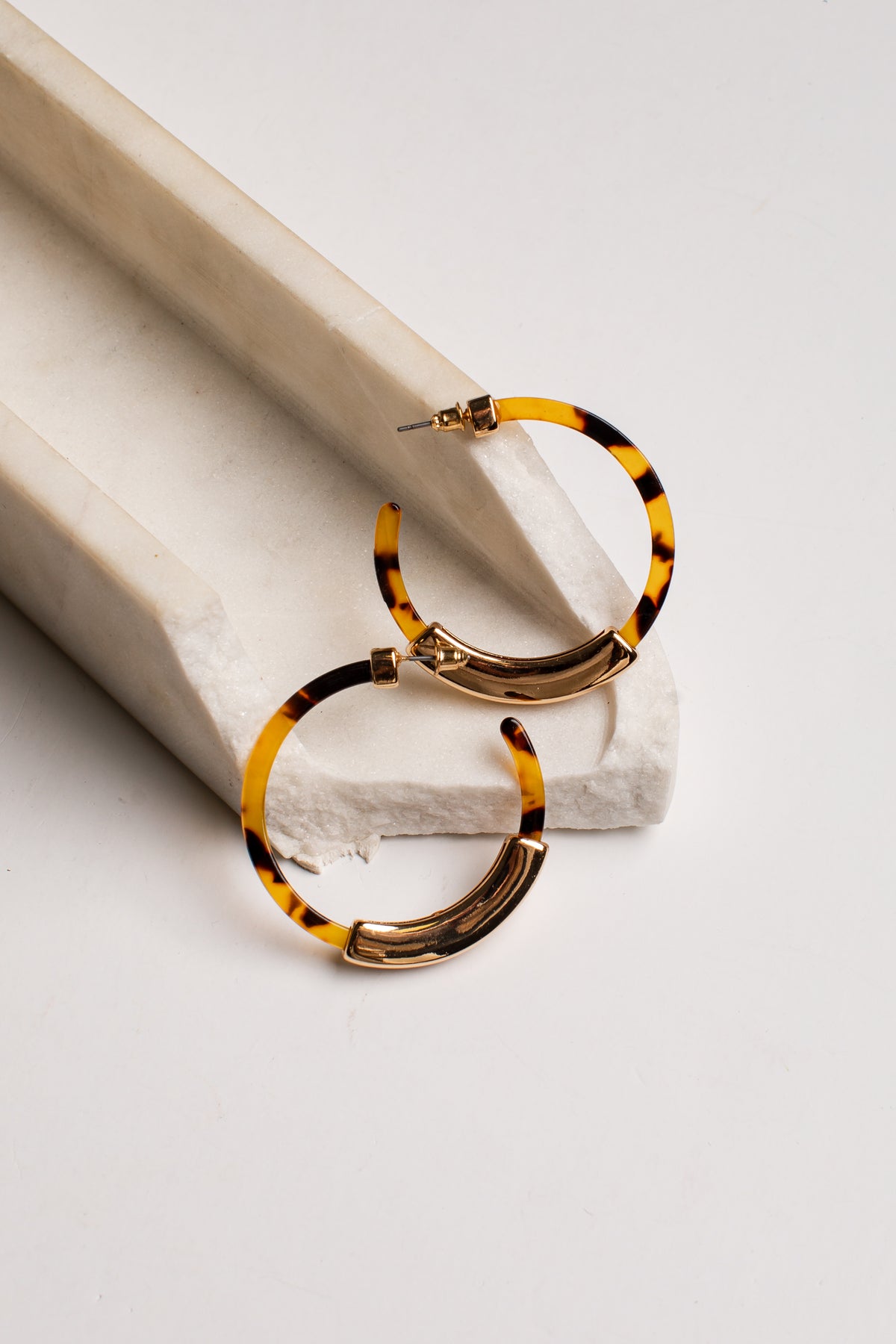 Tortoiseshell hoop earrings with gold-toned metal settings, displayed on a white stone tray against a clean white background.
