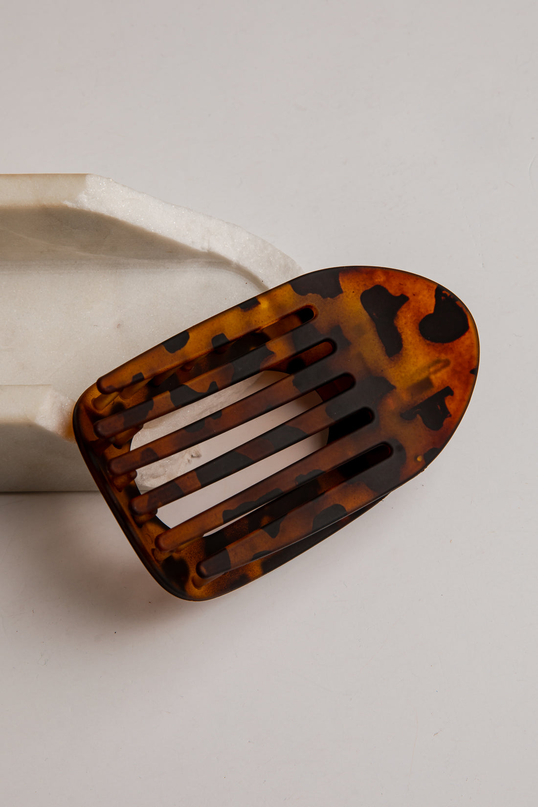A tortoiseshell hair clip with a slotted design, resting on a white ceramic block against a light gray background.