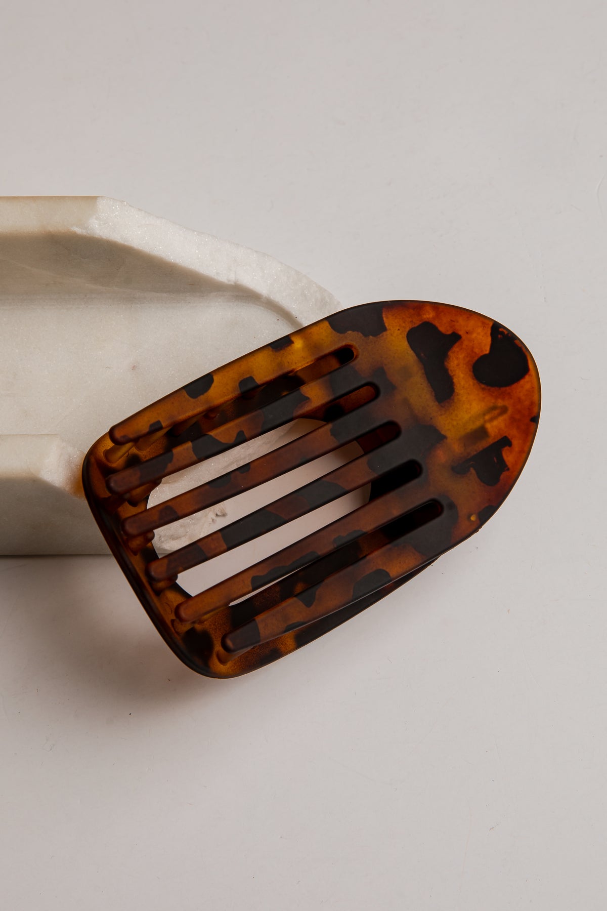 A tortoiseshell hair clip with a slotted design, resting on a white ceramic block against a light gray background.