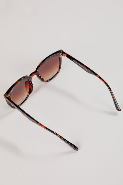 Sunglasses with tortoiseshell frame and brown lenses on a light gray background