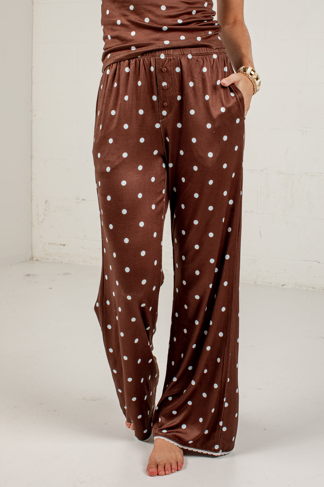 Brown wide-leg pants with a white polka dot pattern, shown on a model standing barefoot against a white wall.