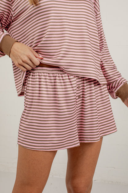A person wearing a matching two-piece loungewear set with a dusty rose and white horizontal stripe pattern, featuring a long-sleeve top and shorts with a button detail.