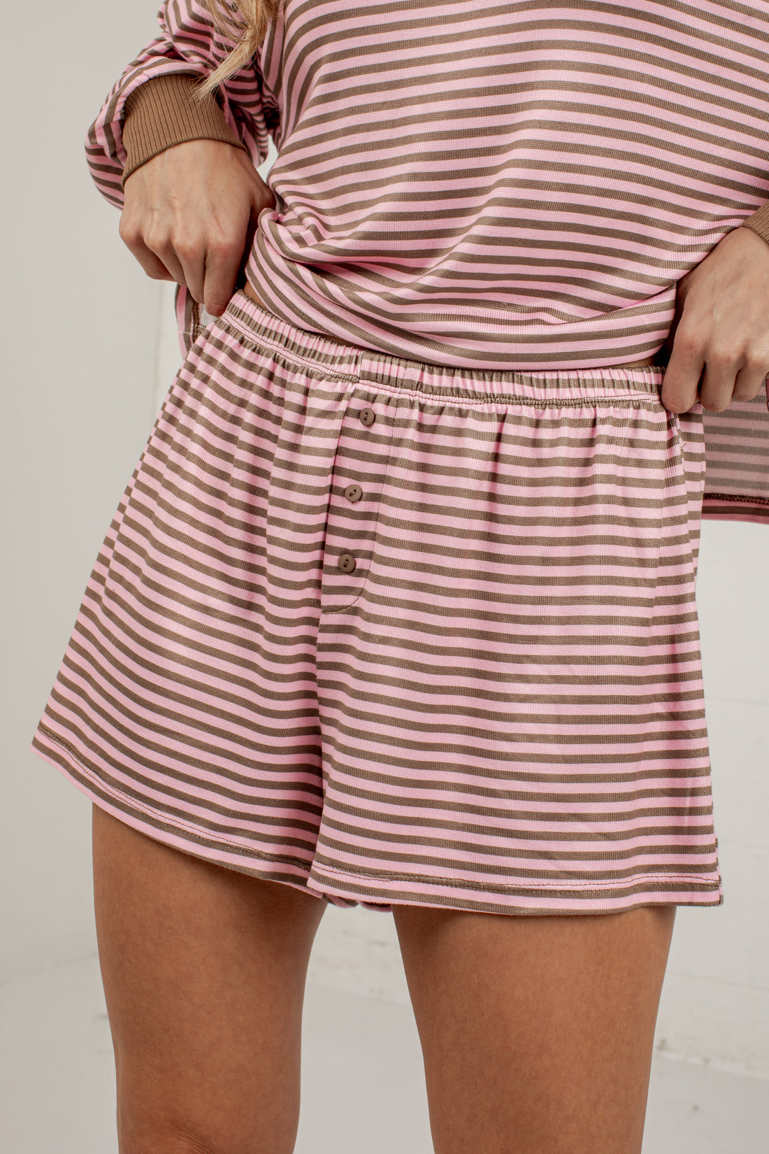 A close-up of a person wearing pink and white striped shorts with a button-front waistband and a matching striped top, photographed against a plain light background.