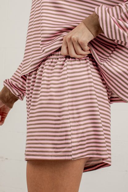 A close-up of a person wearing a matching pink and white striped lounge set, featuring a long-sleeve top with ribbed cuffs and matching shorts with an elastic waistband.