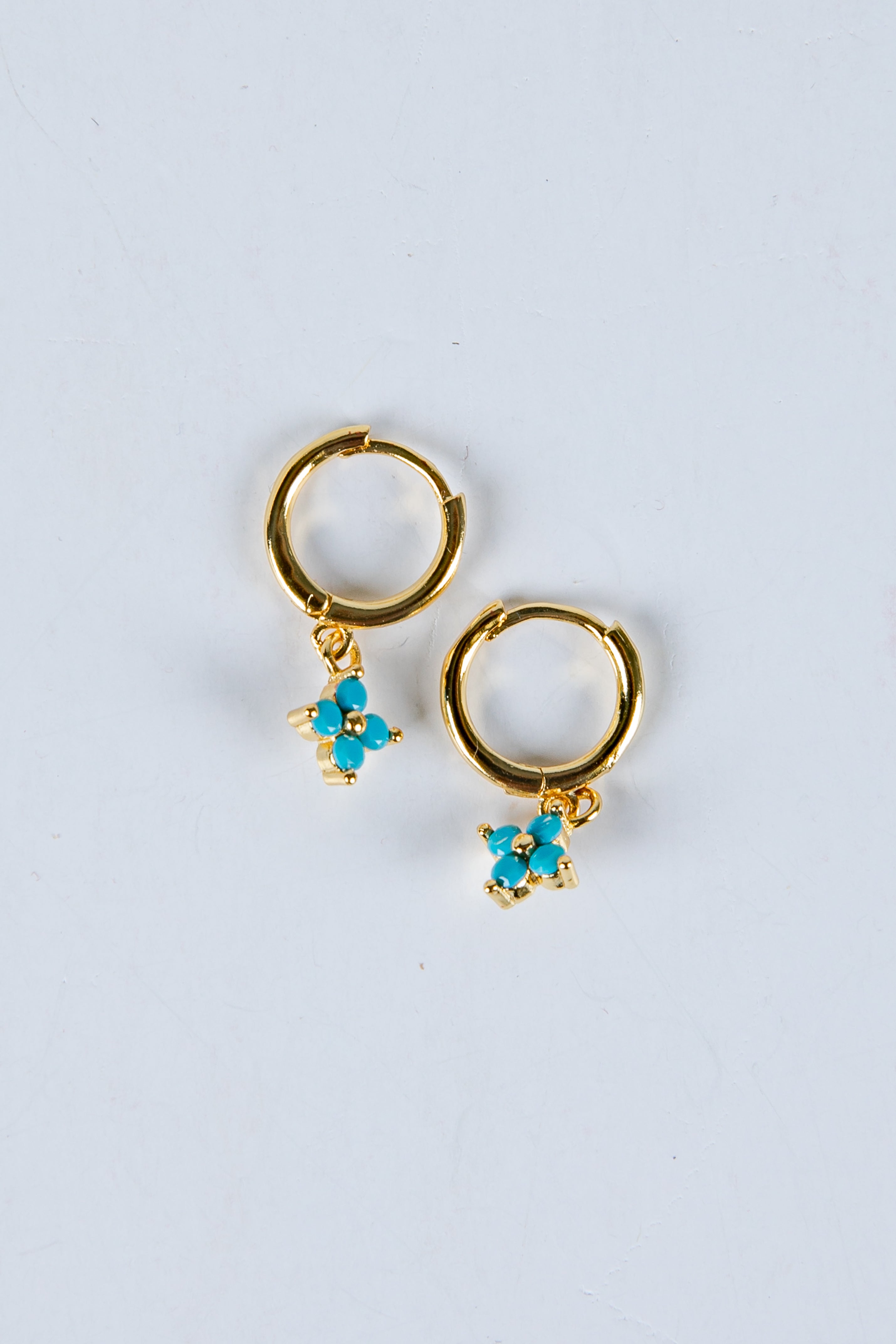 Gold hoop earrings with turquoise flower charms on a light gray background