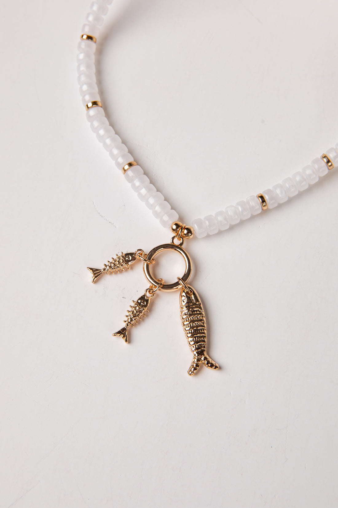 Necklace with white beads and gold fish charms on a light gray background
