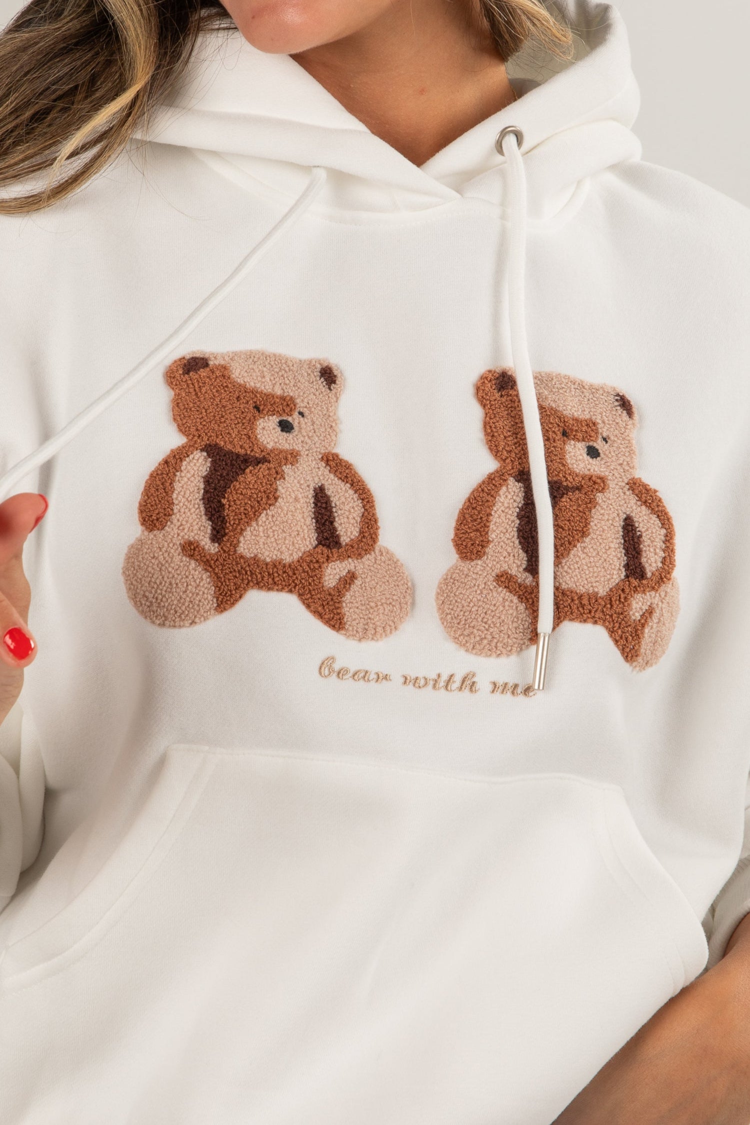 Woman wearing a white hoodie with teddy bear designs on a plain background