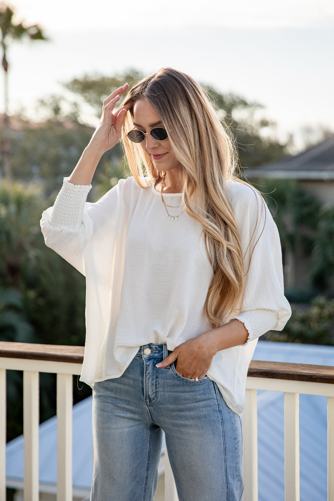 Woman wearing a white blouse and blue jeans standing on a balcony with a blurred background