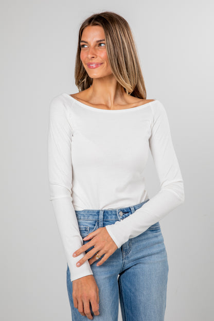 Woman wearing a white long-sleeve top and blue jeans against a gray background