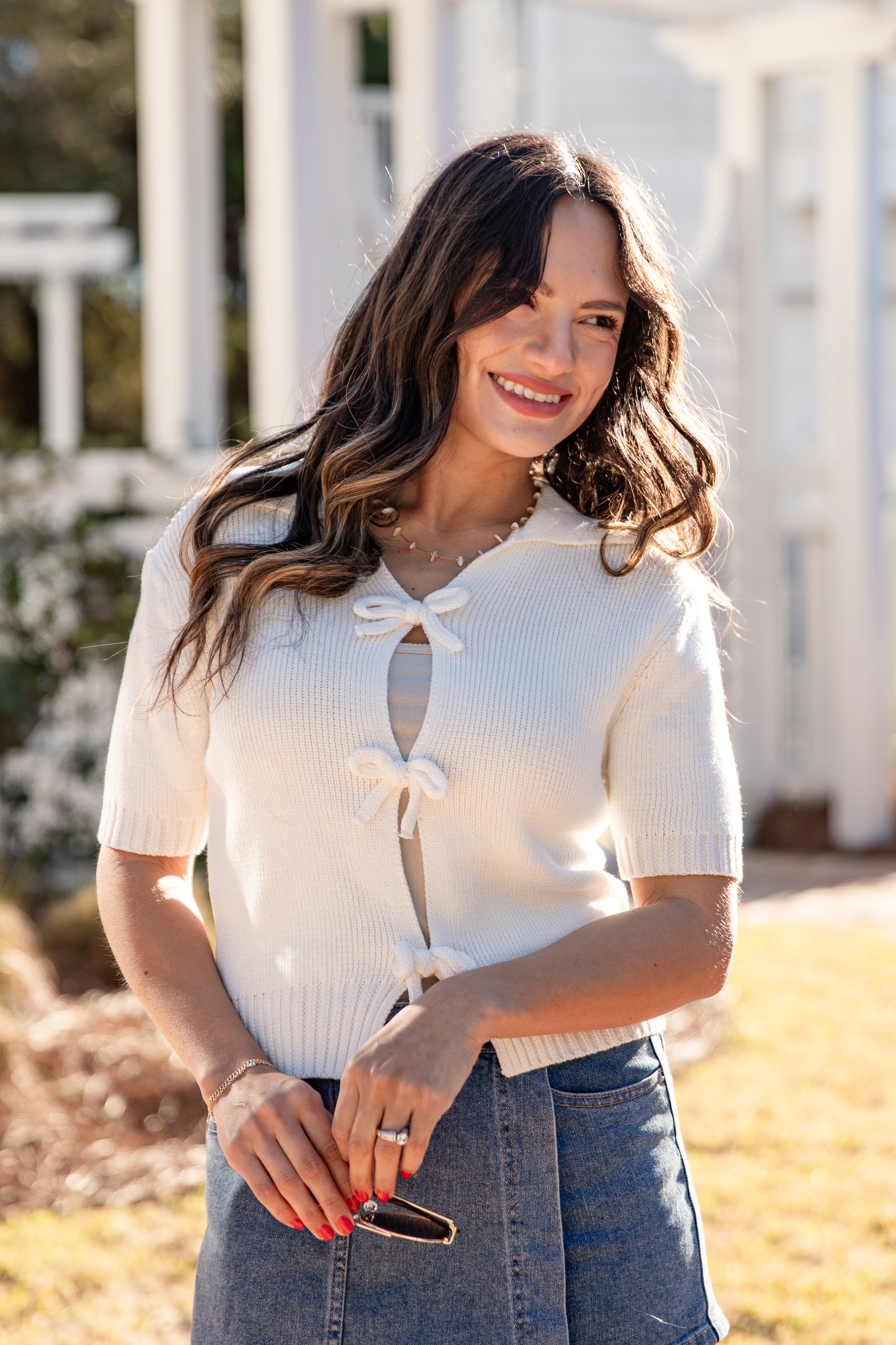 Woman wearing a white short-sleeve top with a bow detail, standing outdoors.