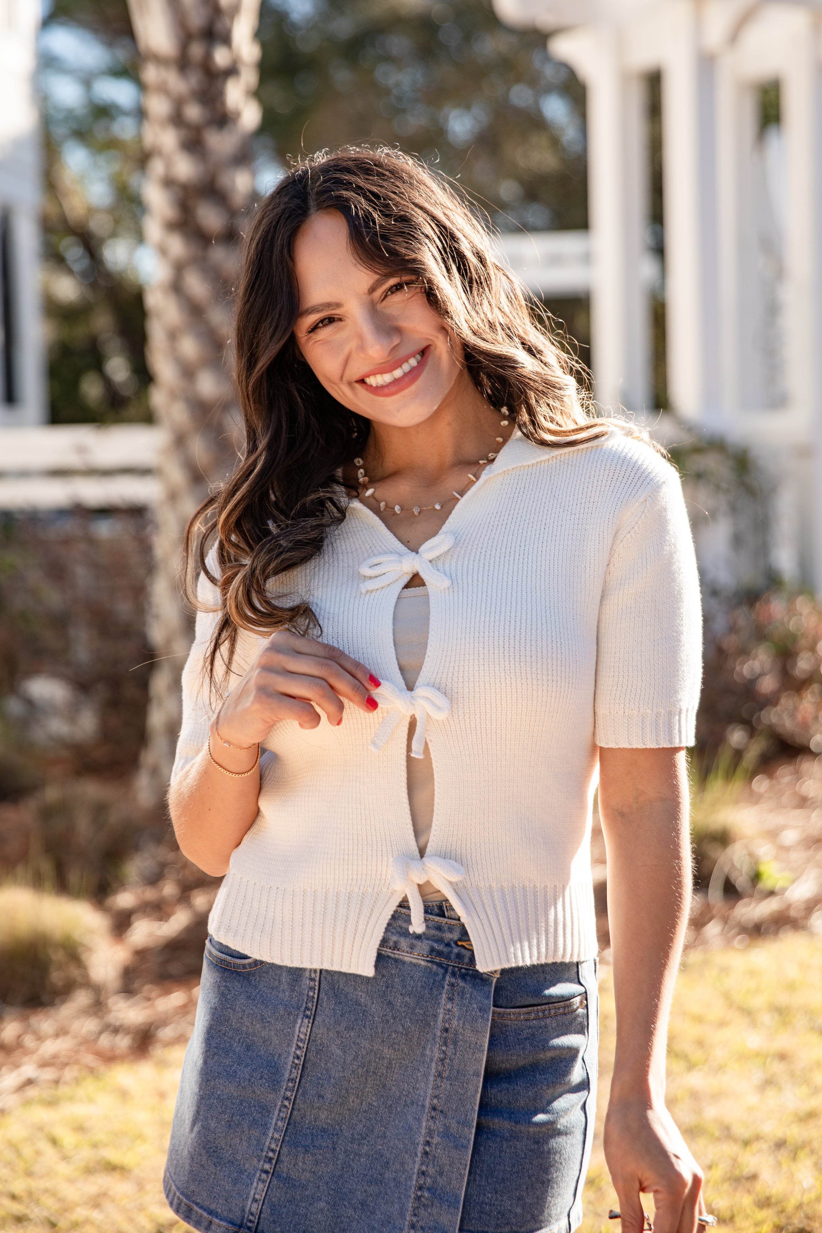 Woman wearing a white knit top with a bow detail outdoors