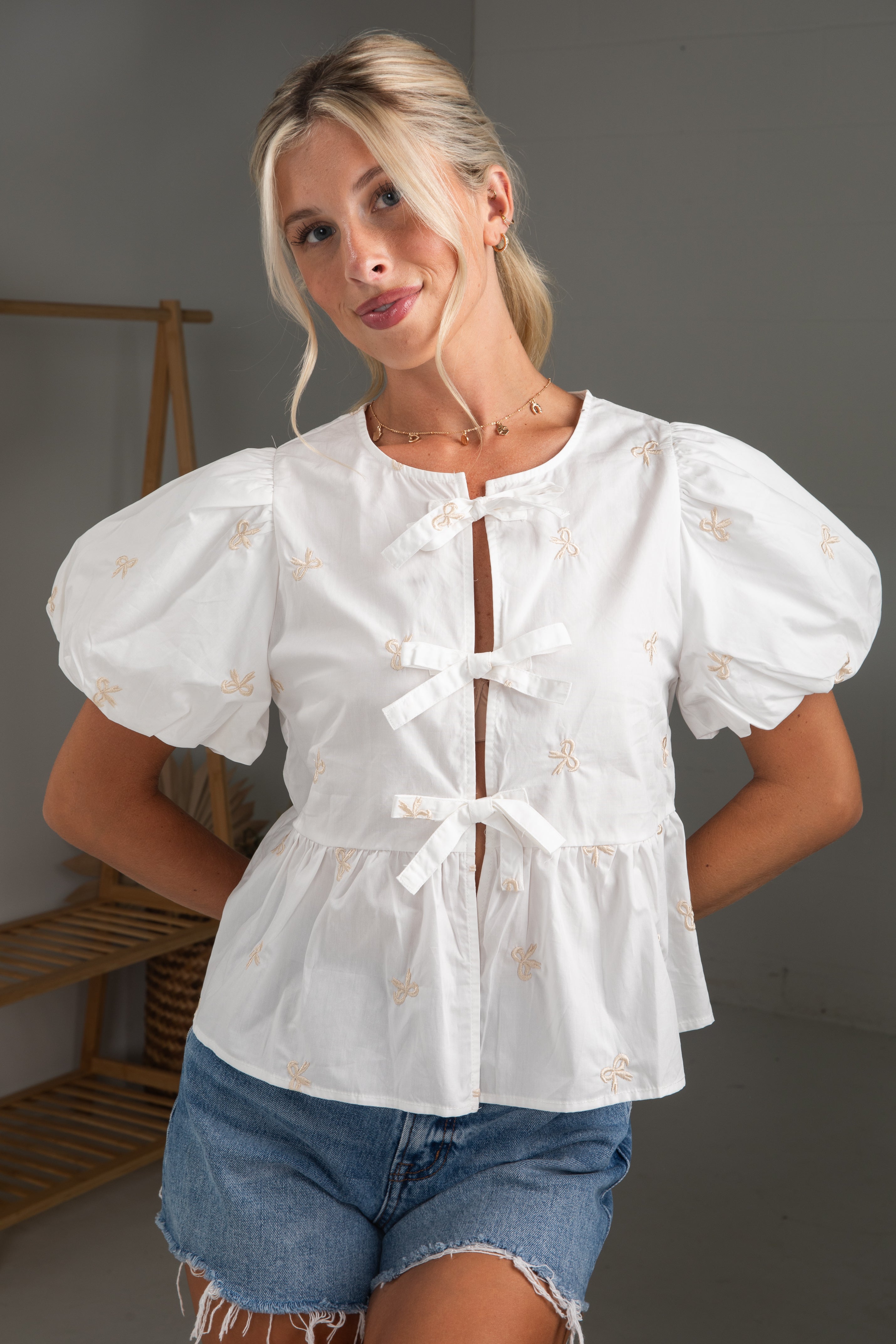 Woman wearing a white blouse with puff sleeves and denim shorts in a neutral setting