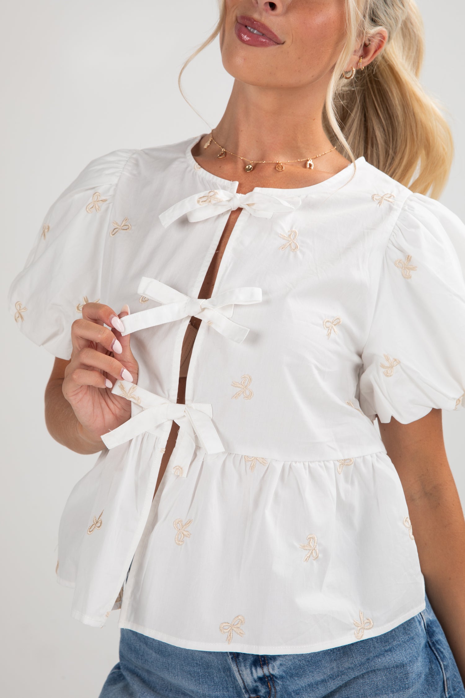 Woman wearing a white blouse with bow details and blue jeans on a plain background
