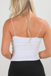 Person wearing a white tank top with thin straps on a plain background