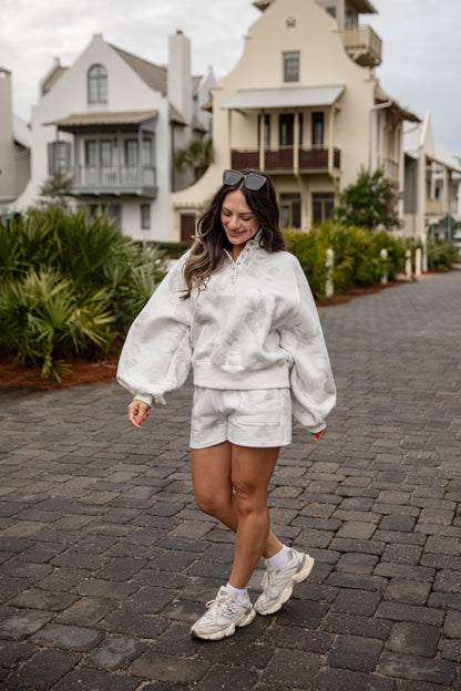 Woman in a white outfit walking on a cobblestone street with houses in the background