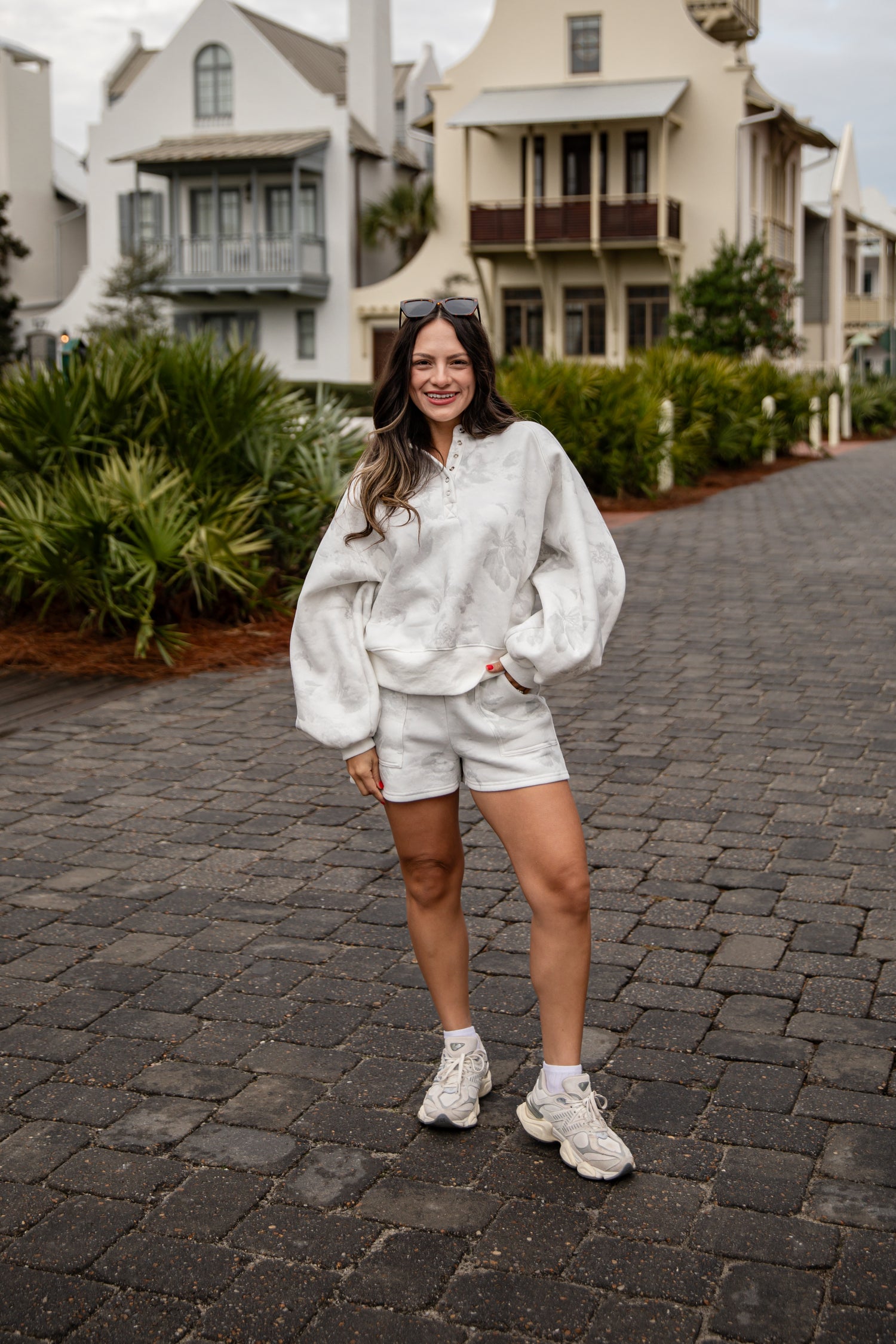 Woman in a white outfit standing on a cobblestone street with houses in the background