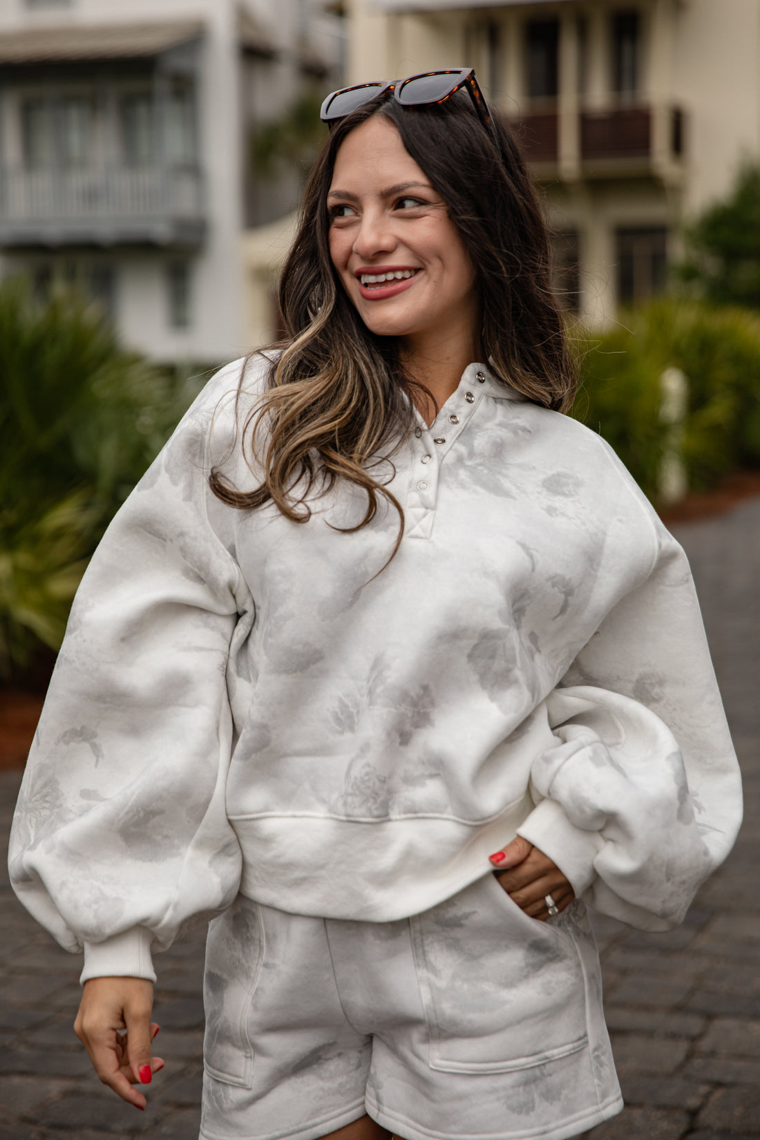 Woman wearing a white marbled outfit with sunglasses on her head, standing outdoors.