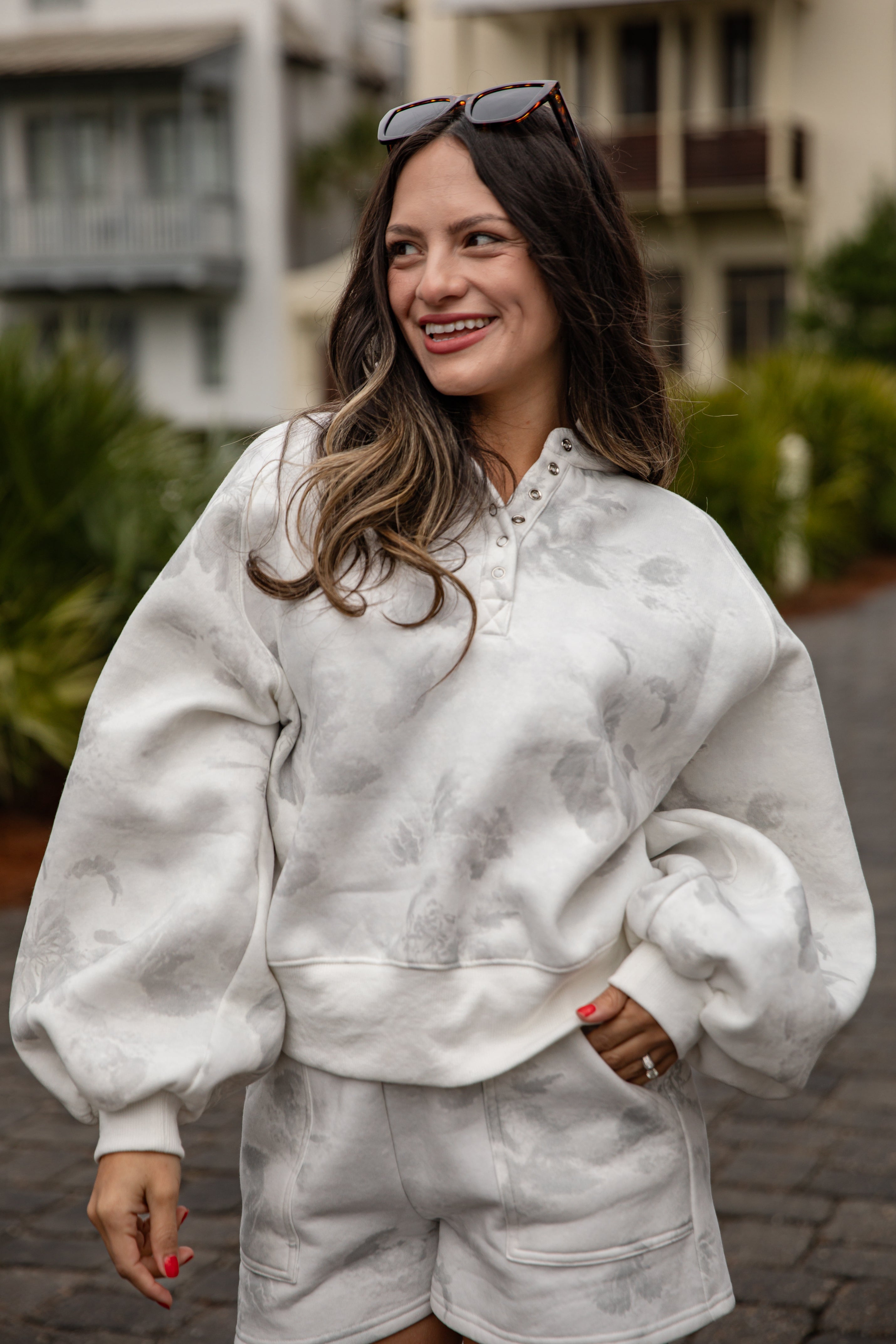 Woman wearing a white marbled outfit with sunglasses on her head, standing outdoors.