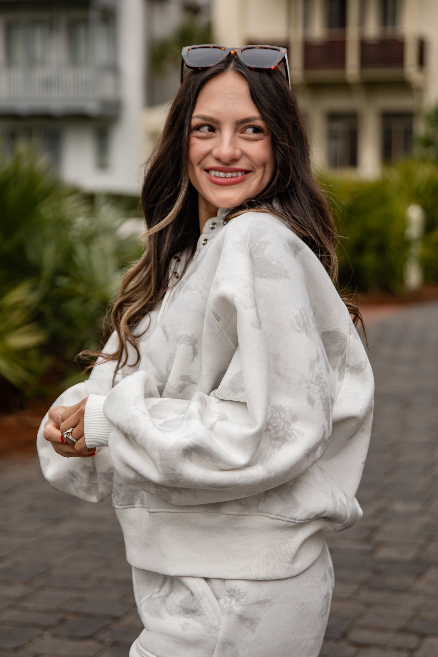 Woman wearing a white sweatshirt and pants with sunglasses on her head, standing outdoors.